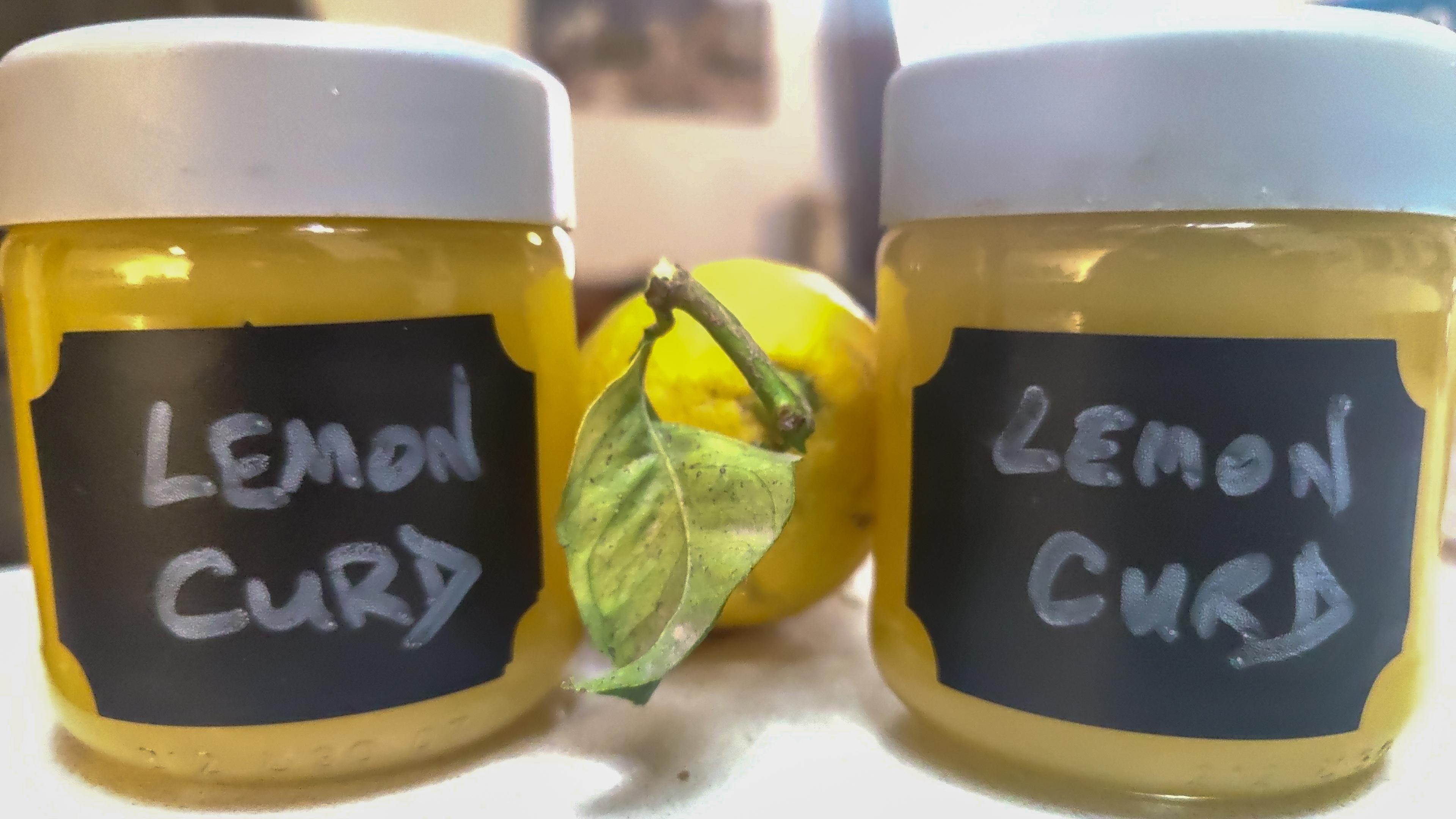 Two jars of homemade lemon curd with a lemon between