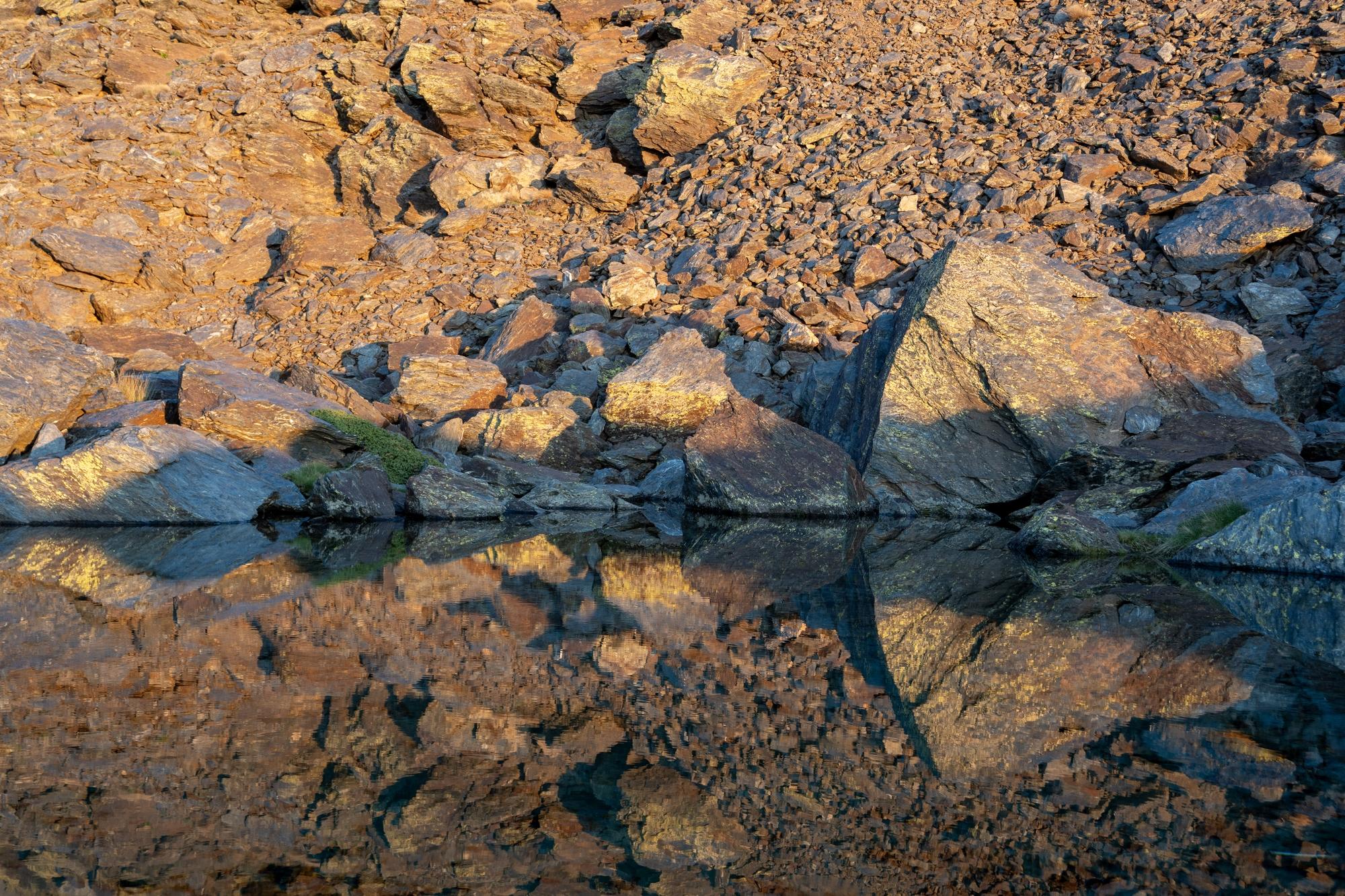A tortured and twisted mountainside is reflected in the waters of a mountain lake