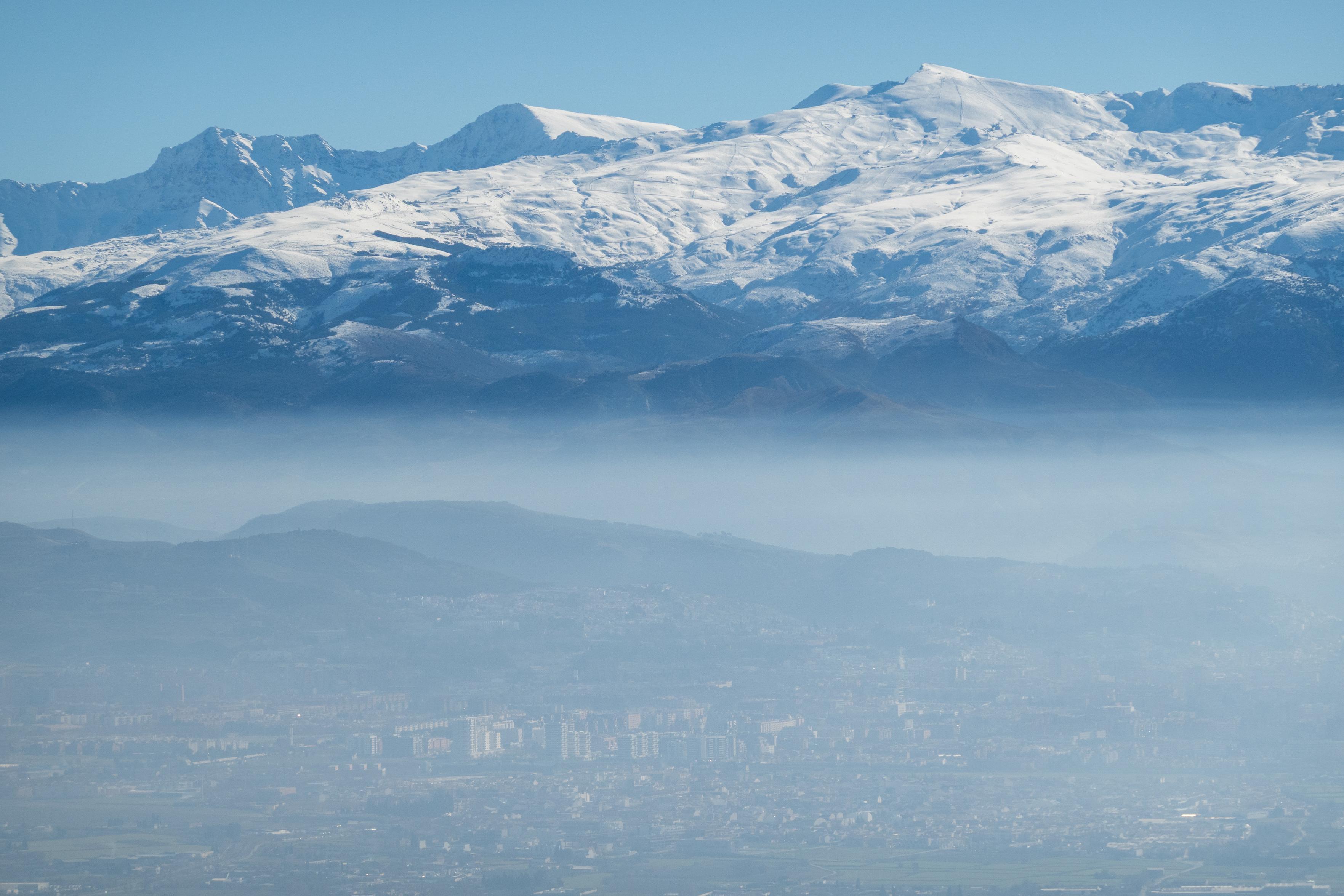 Lower half has outlines of a city in haze, the upper have snow covered mountains
