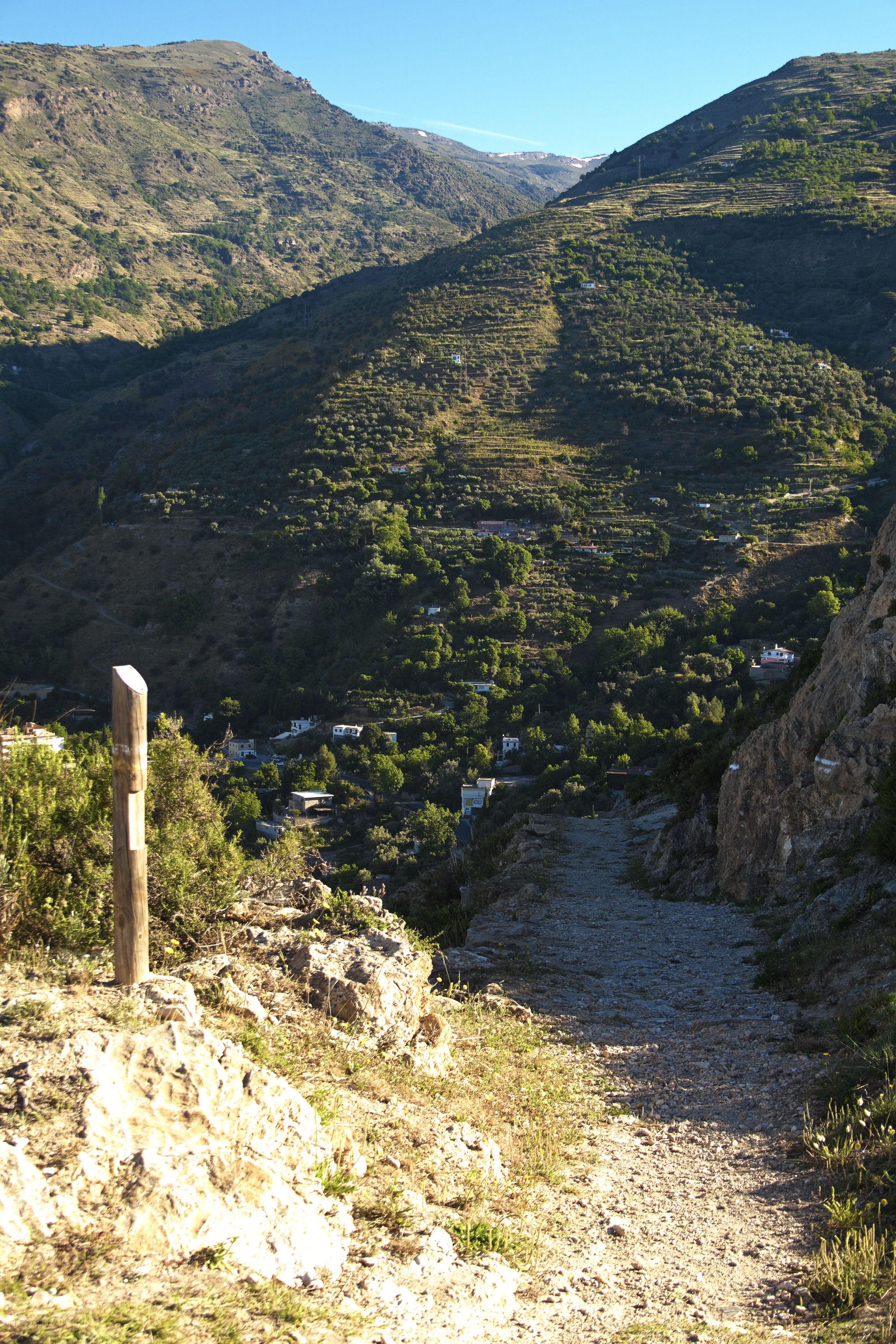 A path marked by a post descends off to the right. In the distance some lovely green hillsides and mountainsides with deep valleys