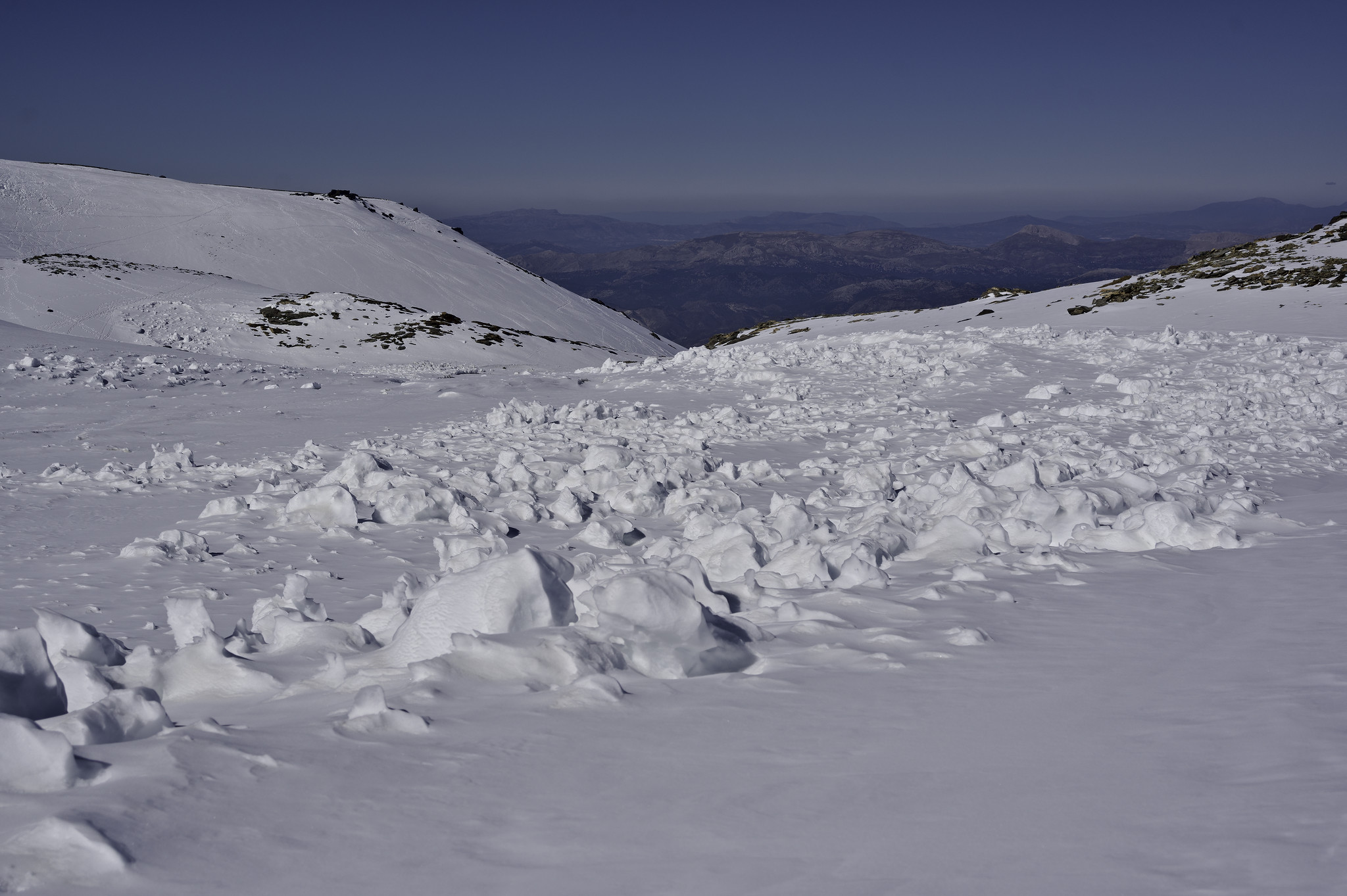 Blocks of snow remain on a level snow covered plateau. Blue sky above