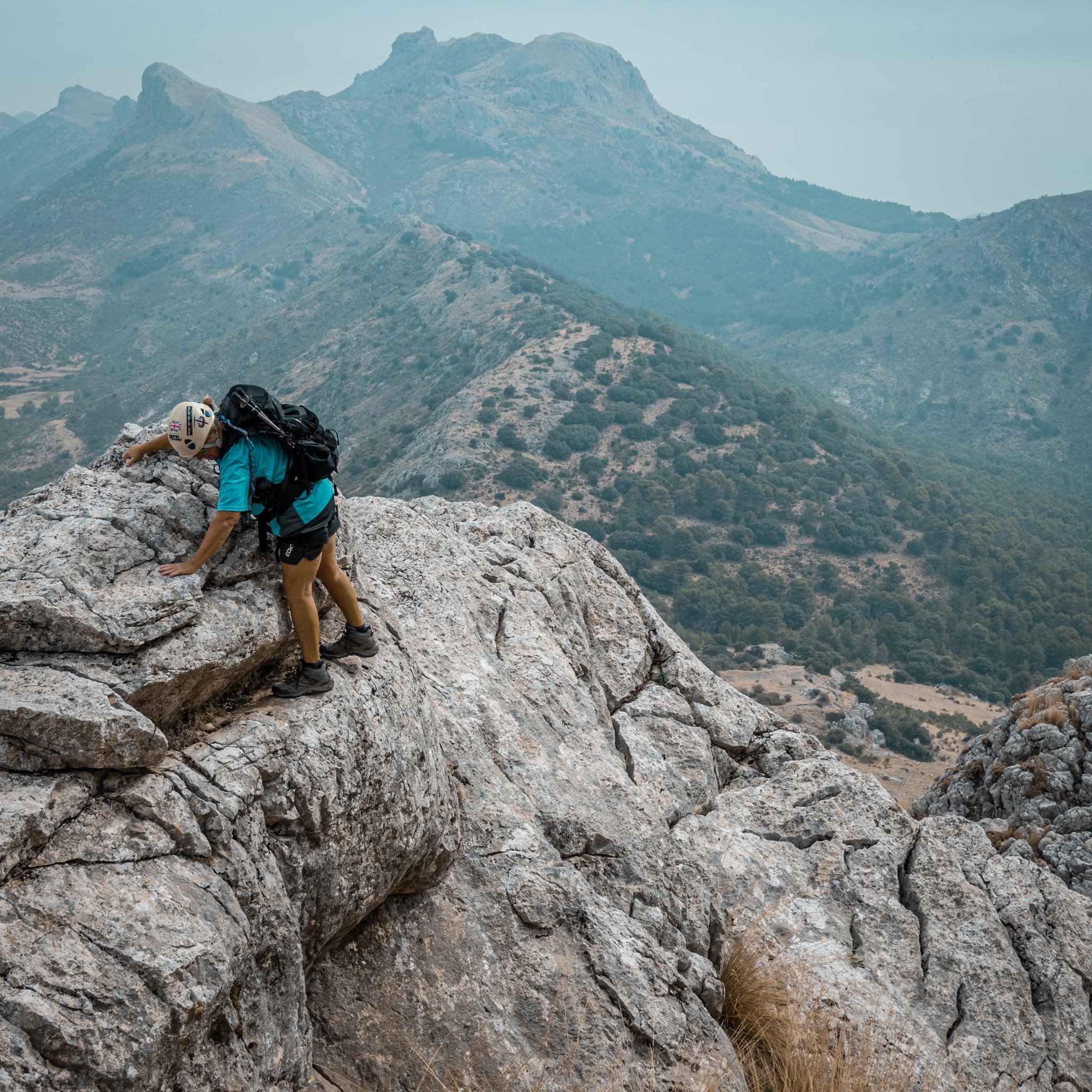 A person in light blue edges around a narrow ledge above a big drop