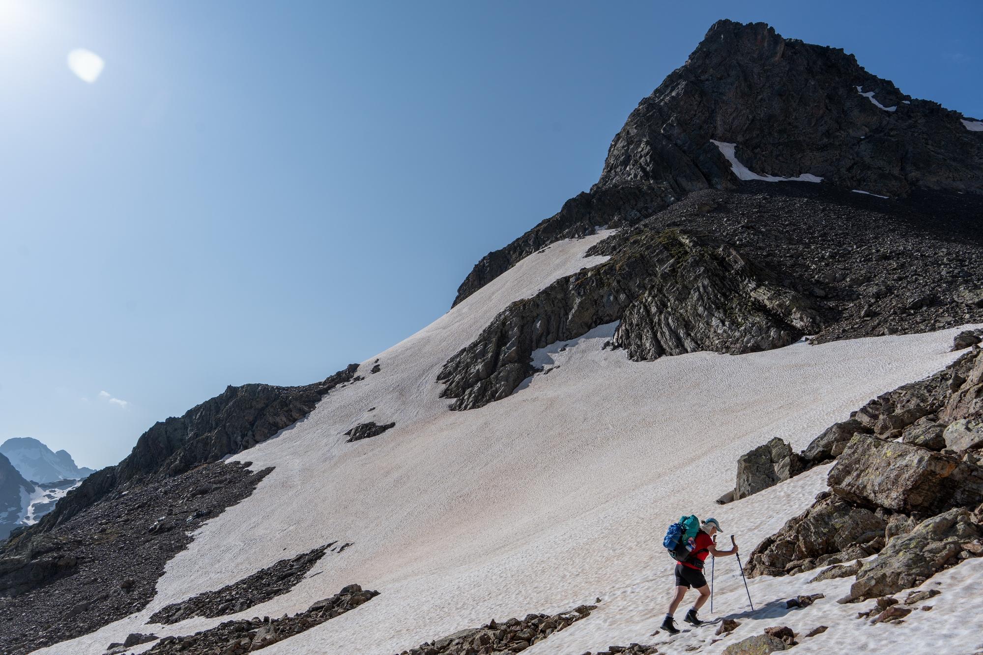 A person is crossing a snowfield in the bottom right of the photo. Behind rises a rocky mountain peak