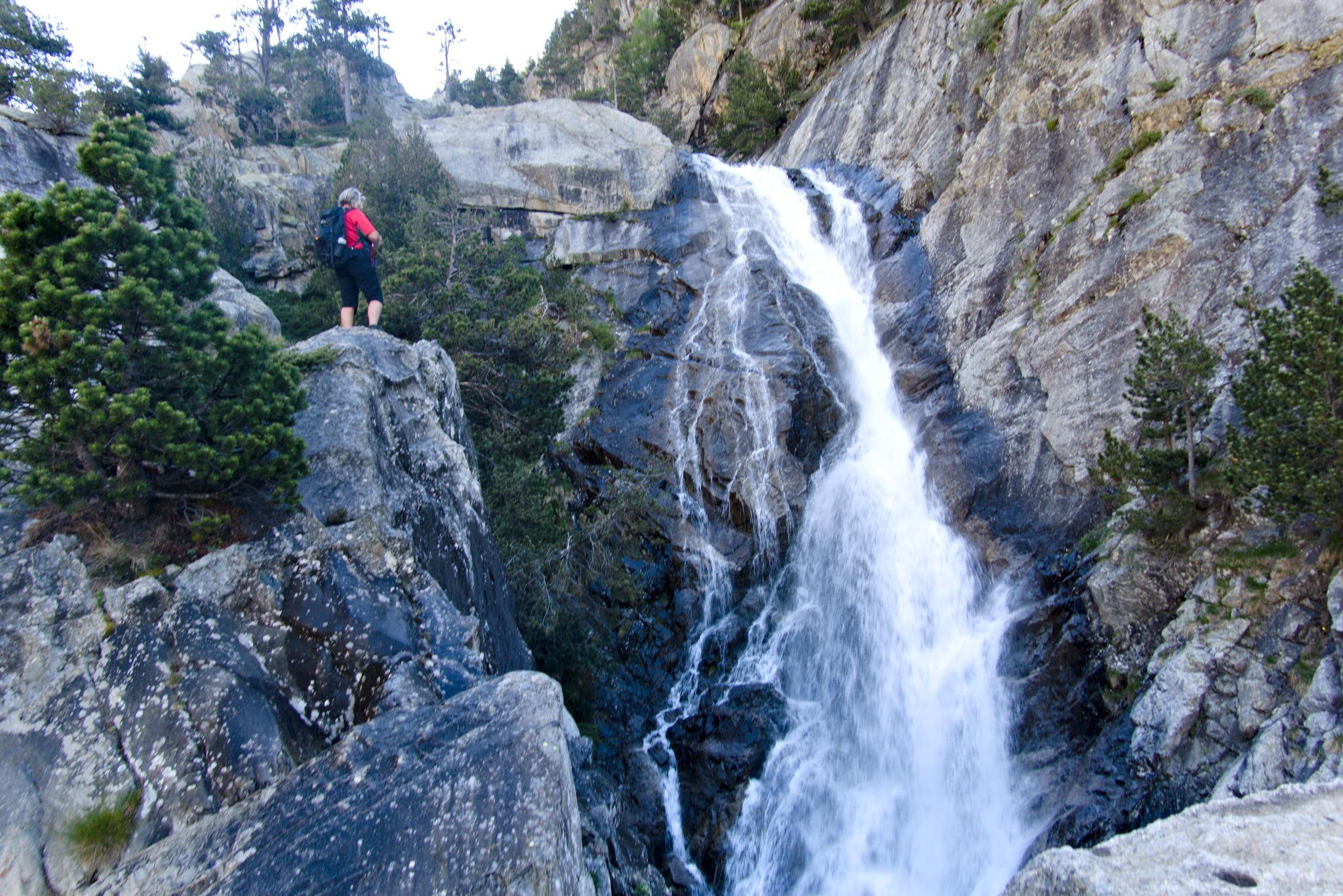 A person in red stands alongside a large waterfall