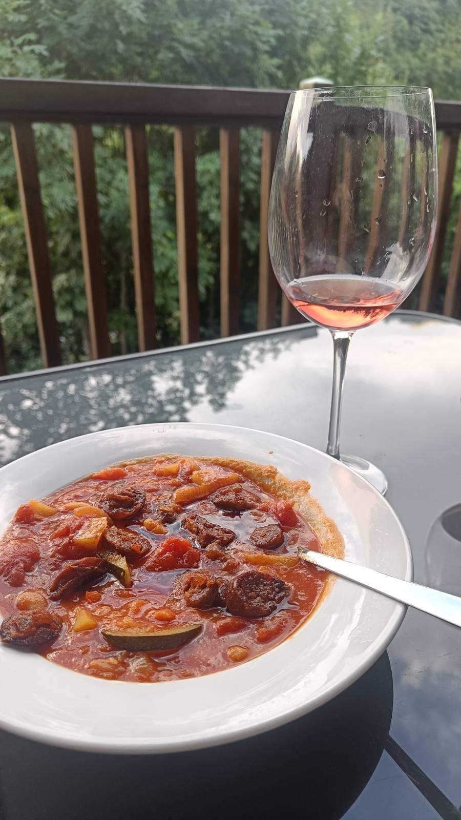 Traditional Spanish meal of potato, pepper and chorizo stew on a plate. A glass of rose wine behind