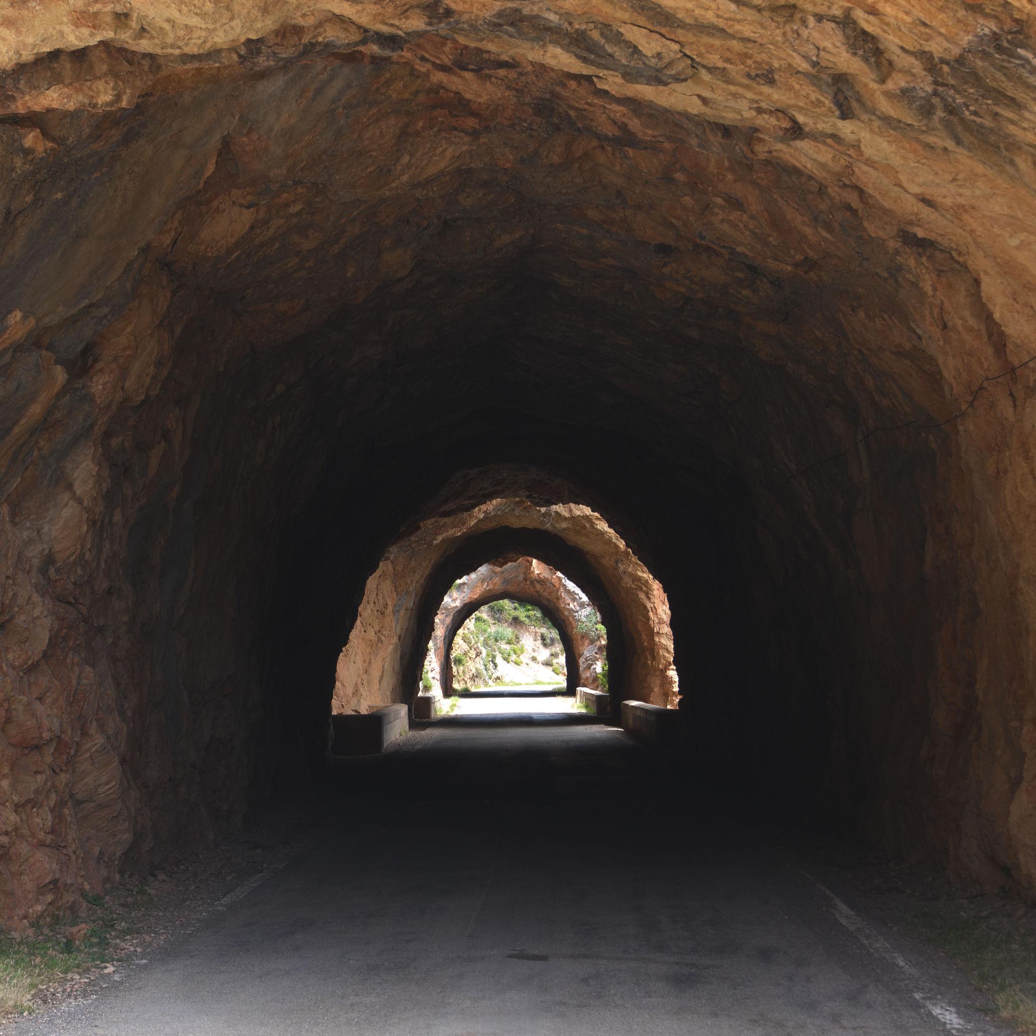 A series of tunnels intermittently lit by sunlight getting smaller as they become more distant. The rock is orange colored.