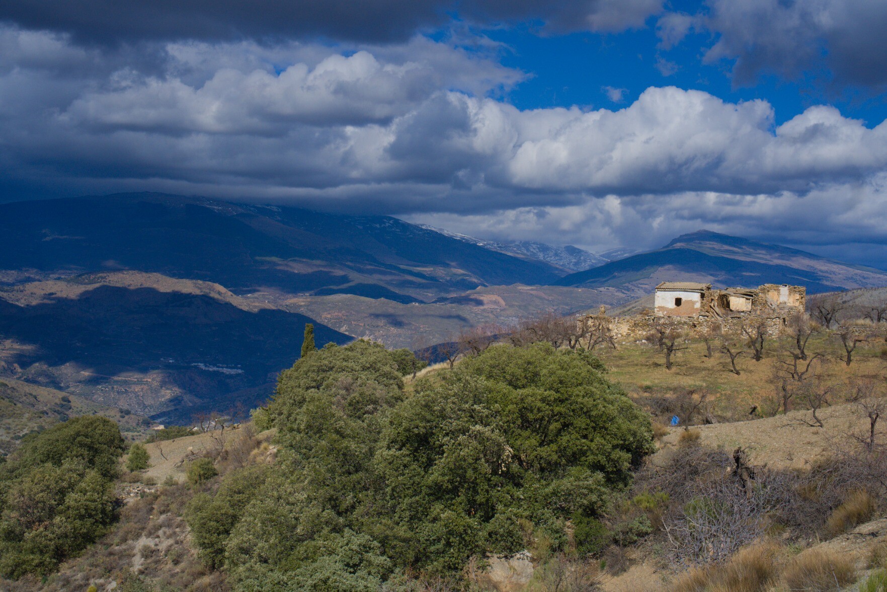 Rural cottage in southern Spain set on a hill with dark, ominous clouds massing beyond in the snowy mountains