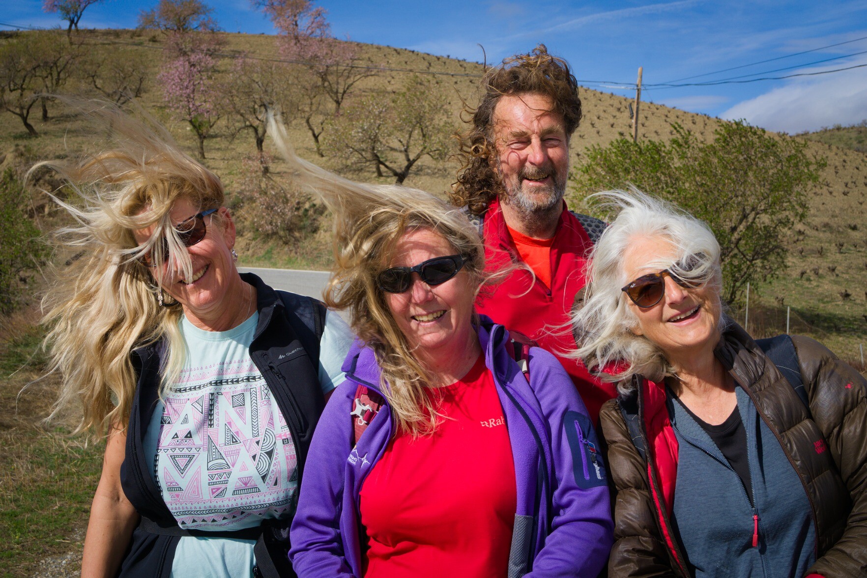 4 people in the hills of Spain and their hair being blown about in the strong wind.