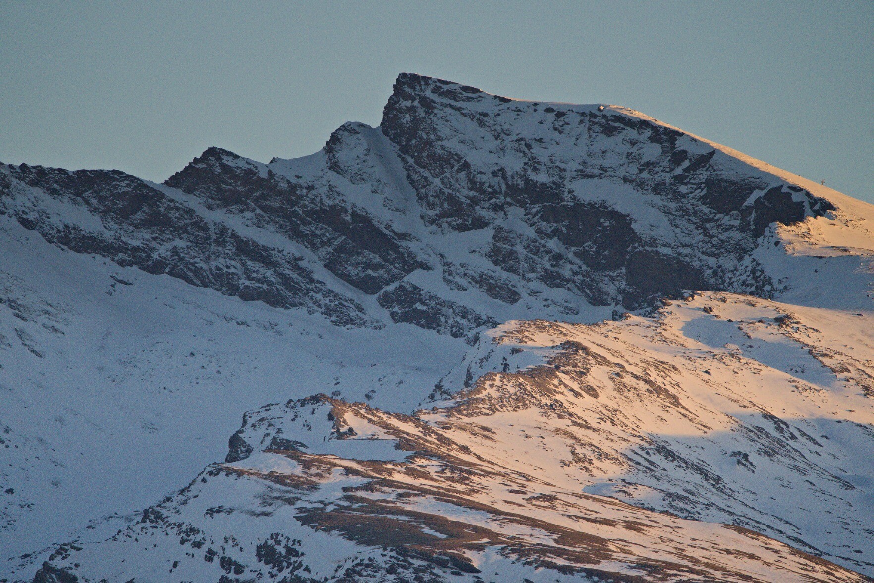 The peak of Veleta, a steep northern mountain face covered in snow. Late afternoon sunlight shines to the right