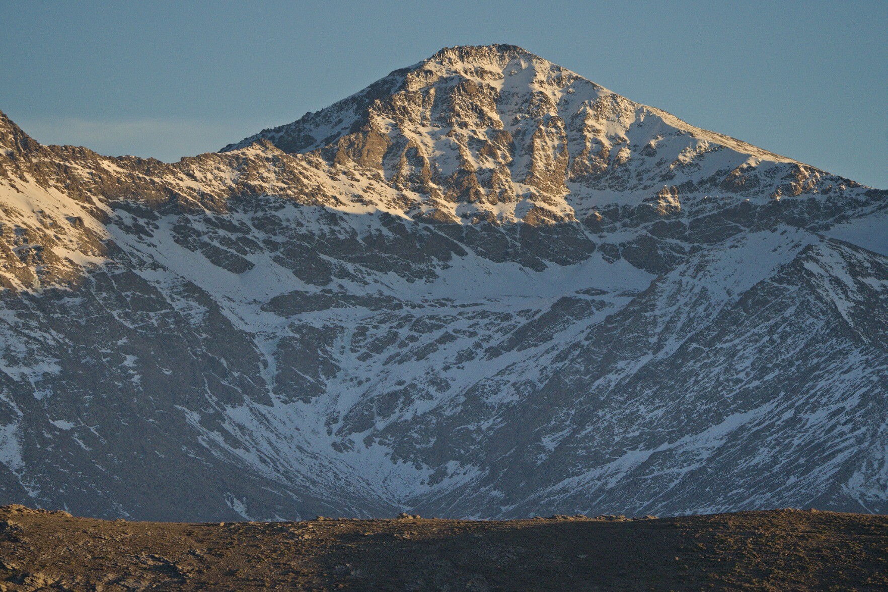 The peak of Mulhacen, a steep northern mountain face covered in snow with late afternoon sunlight hitting the upper part of the mountain