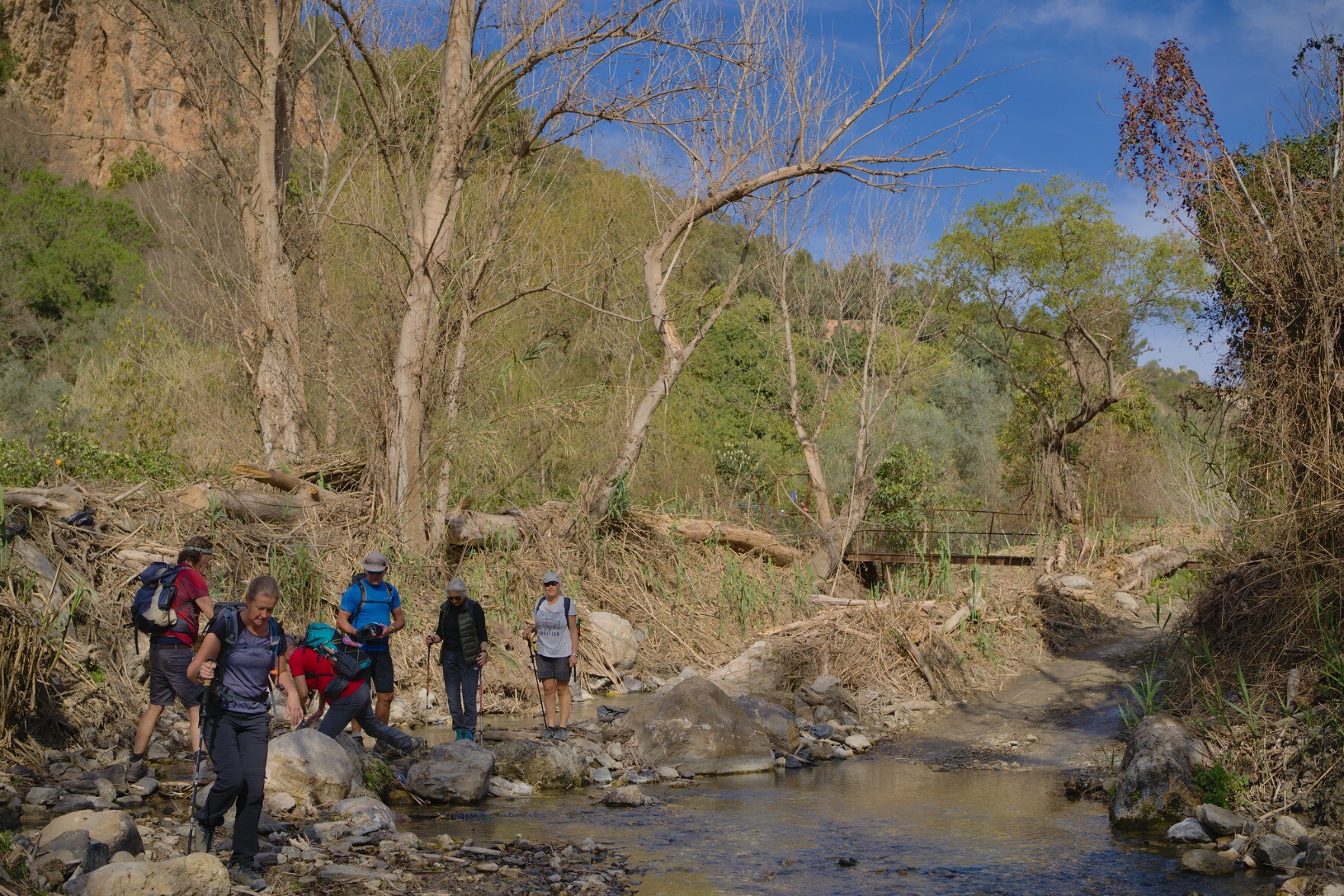 Hikers negotiating a way alongside a river. Blue skies above