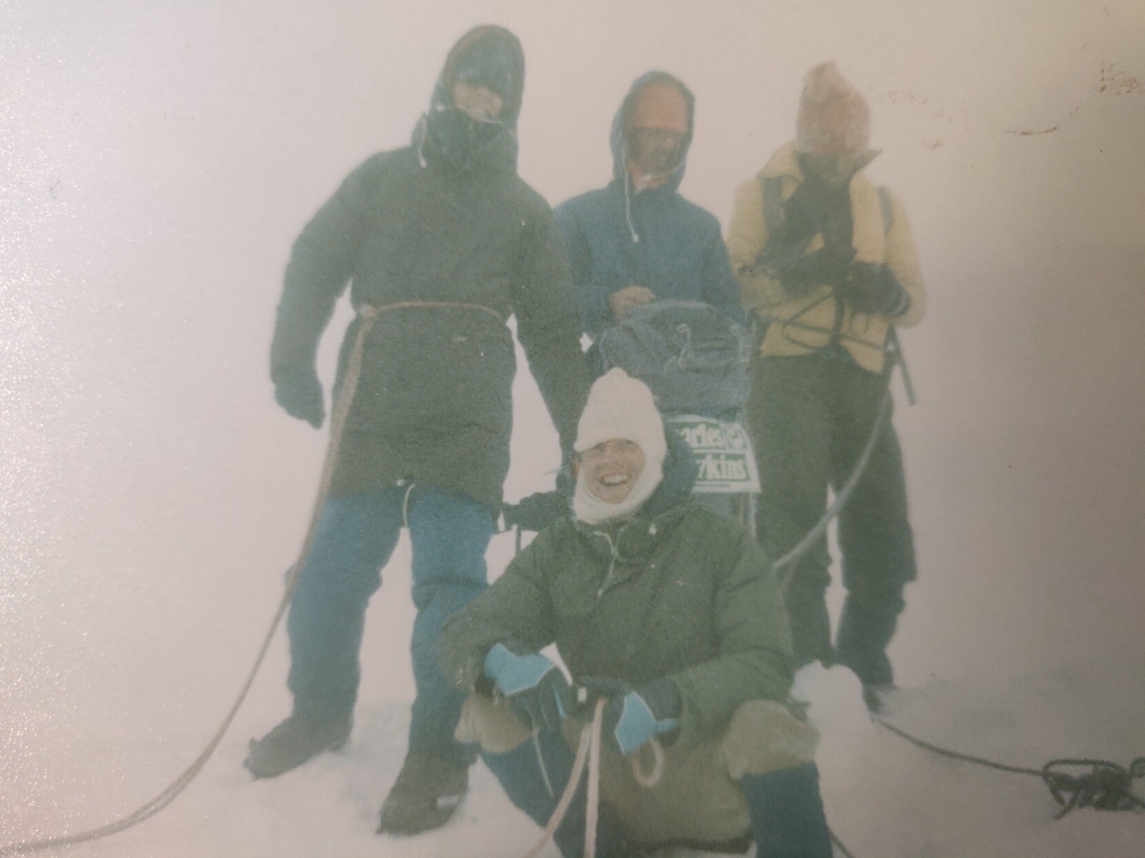 4 mountaineers stand on the summit of Mont Blanc in the Alps, in thick fog, surrounded by snow