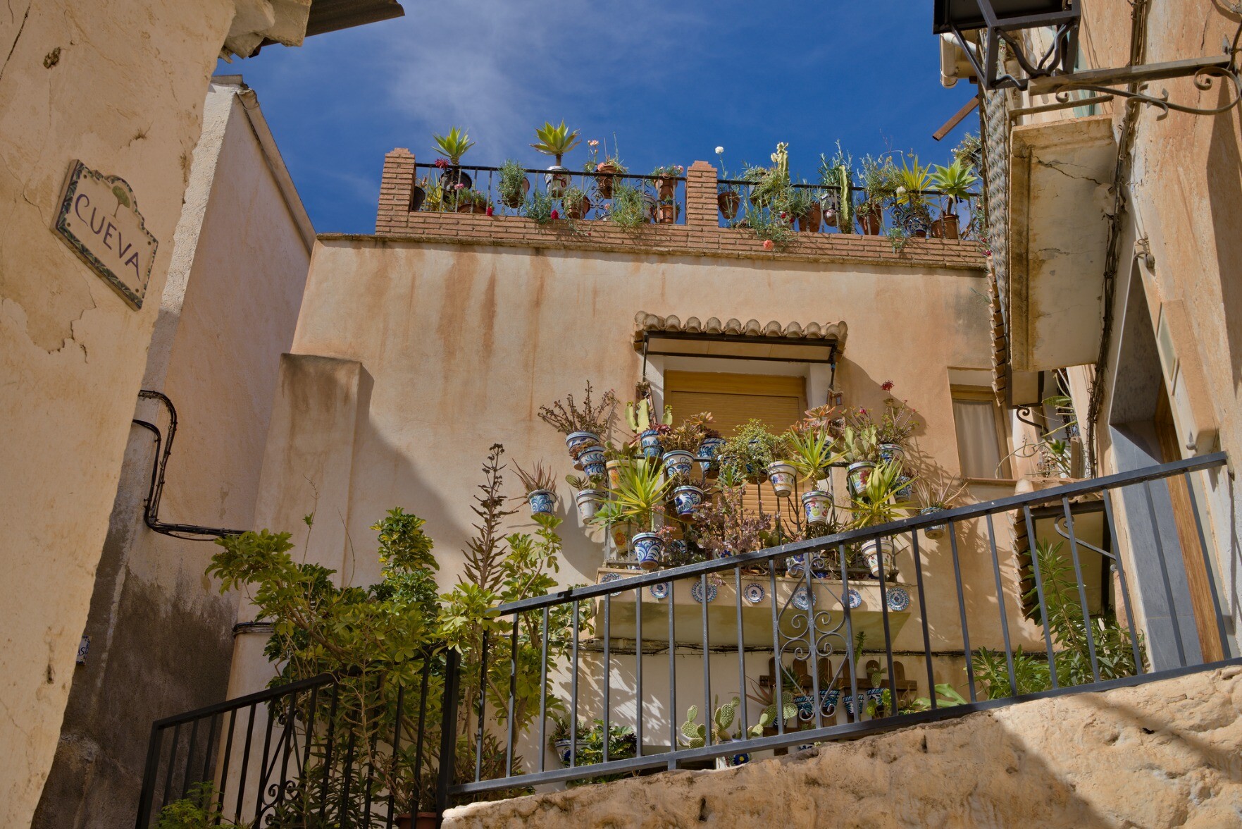 A typical town house in southern Spain with rather drab paint decorated with plants and shrubs in ceramic vases. Blue sky above