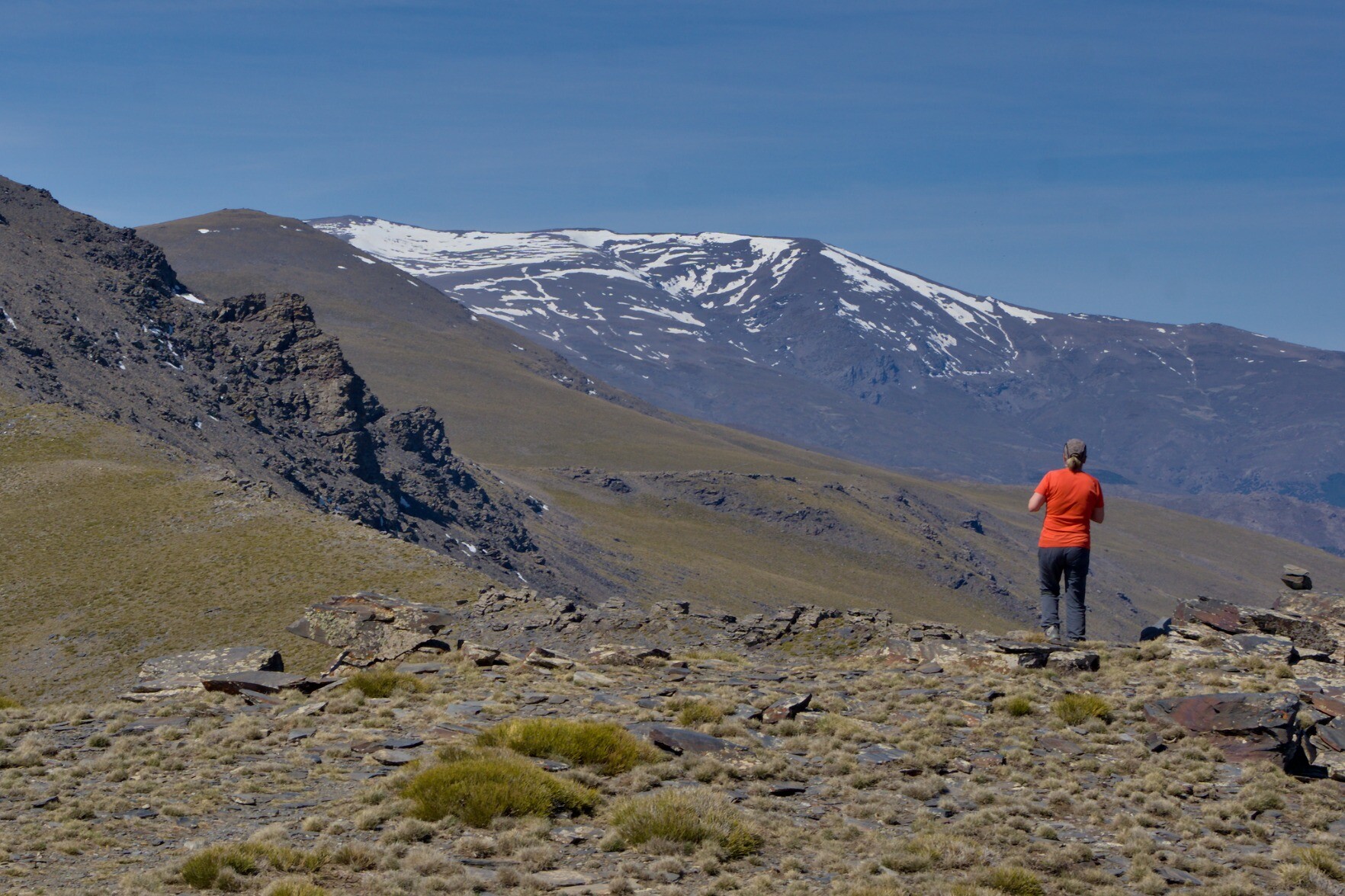 The Picos de Jerez in Spain's Sierra Nevada with snow on it. In the foreground a solitary hiker looks at the view