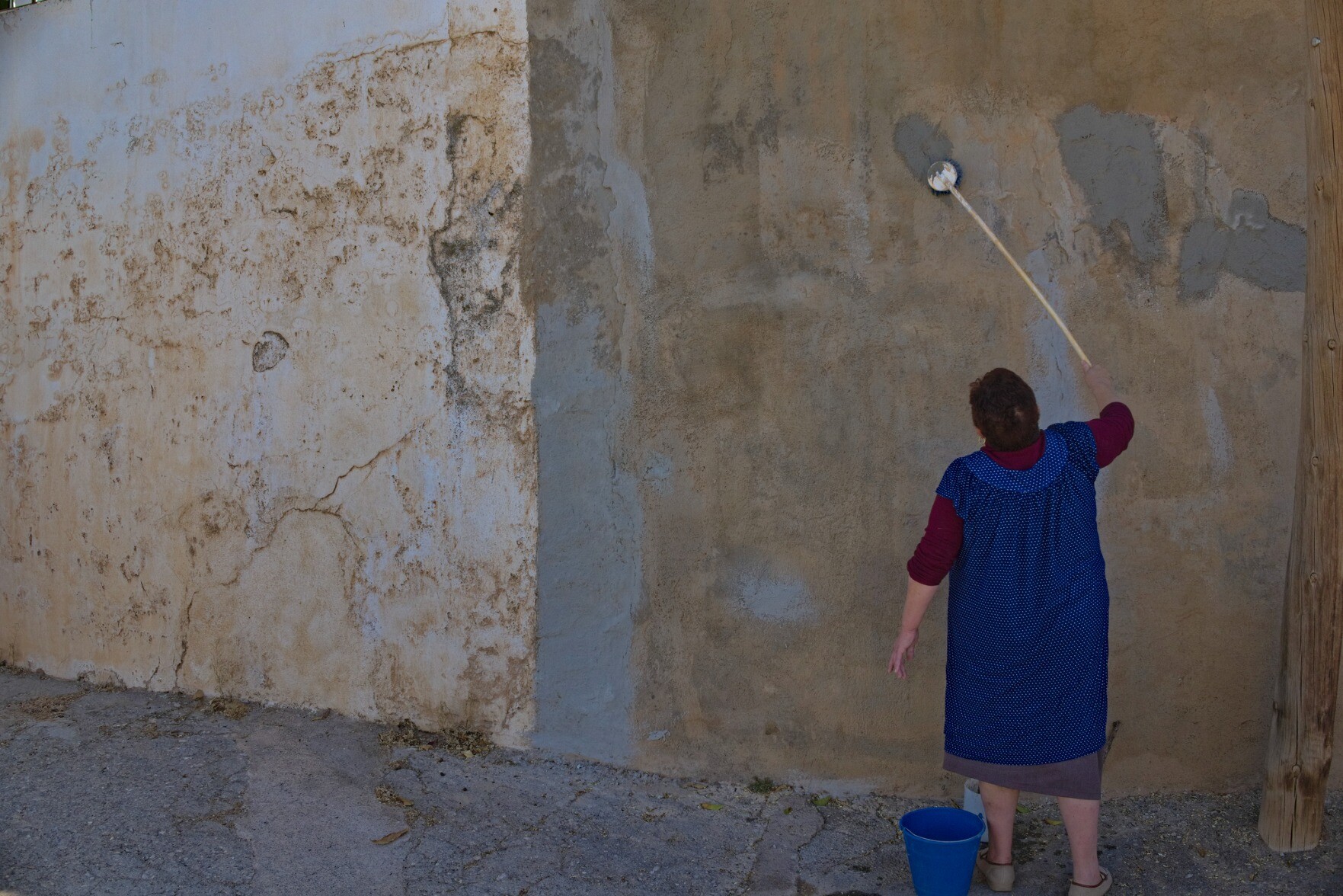 A lady scrubs and repairs a broken wall using a brush