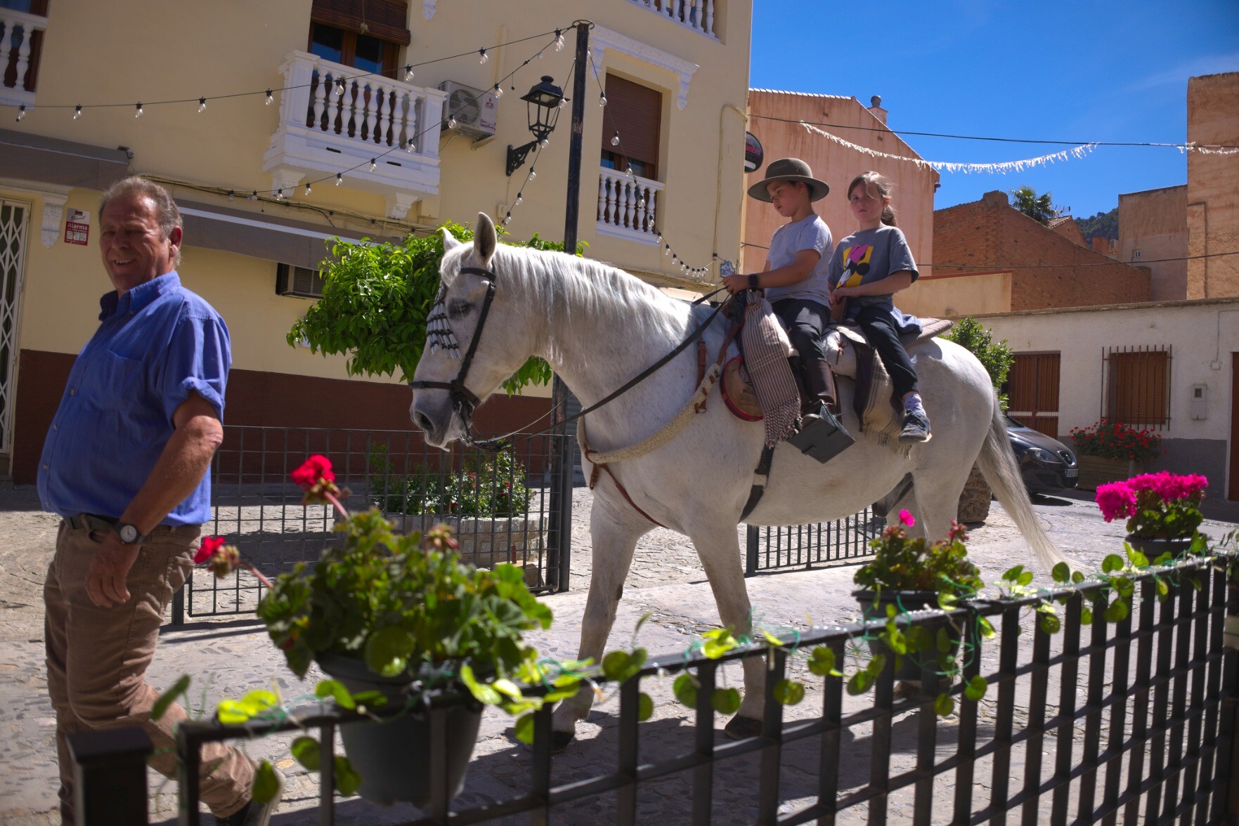 Two children sit on a white horse in the middle of the town of Niguelas, Andalucia