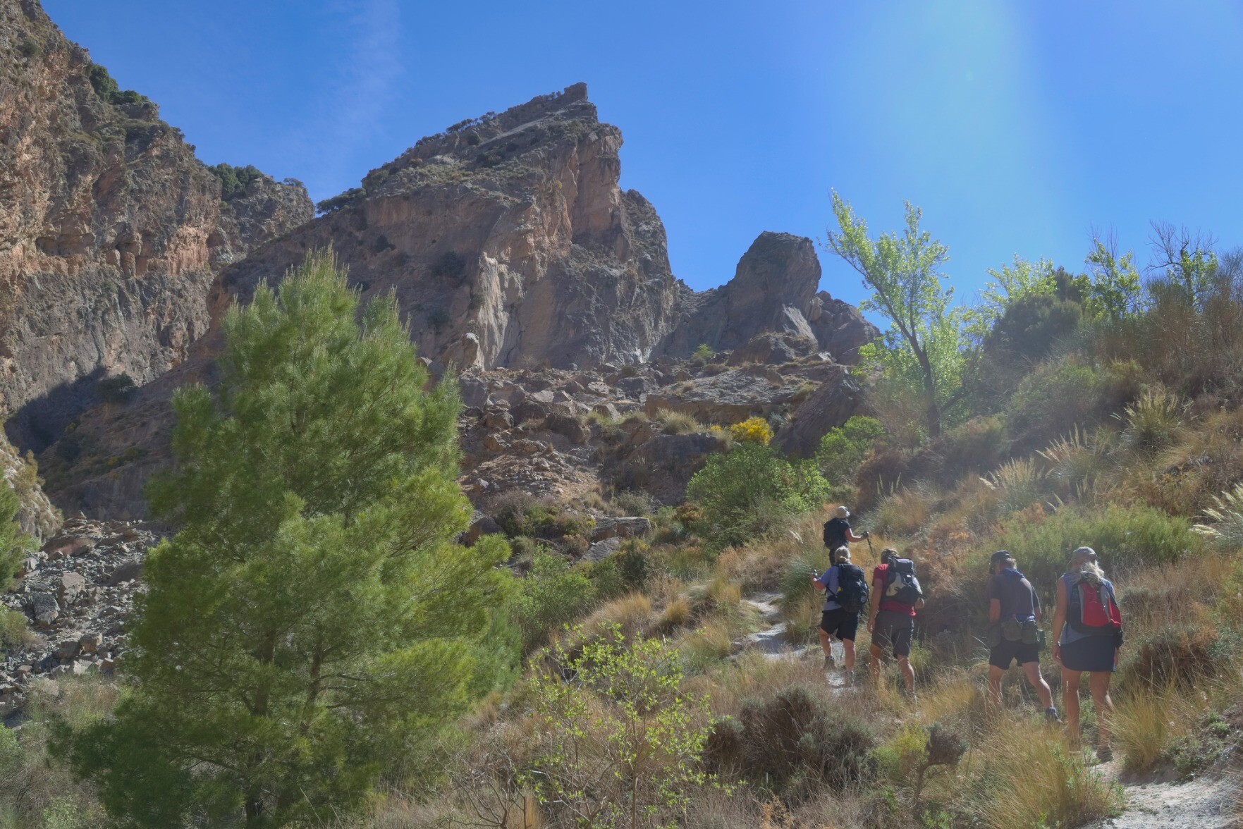 A group of hikers walk beneath a prominent rocky mountain summit