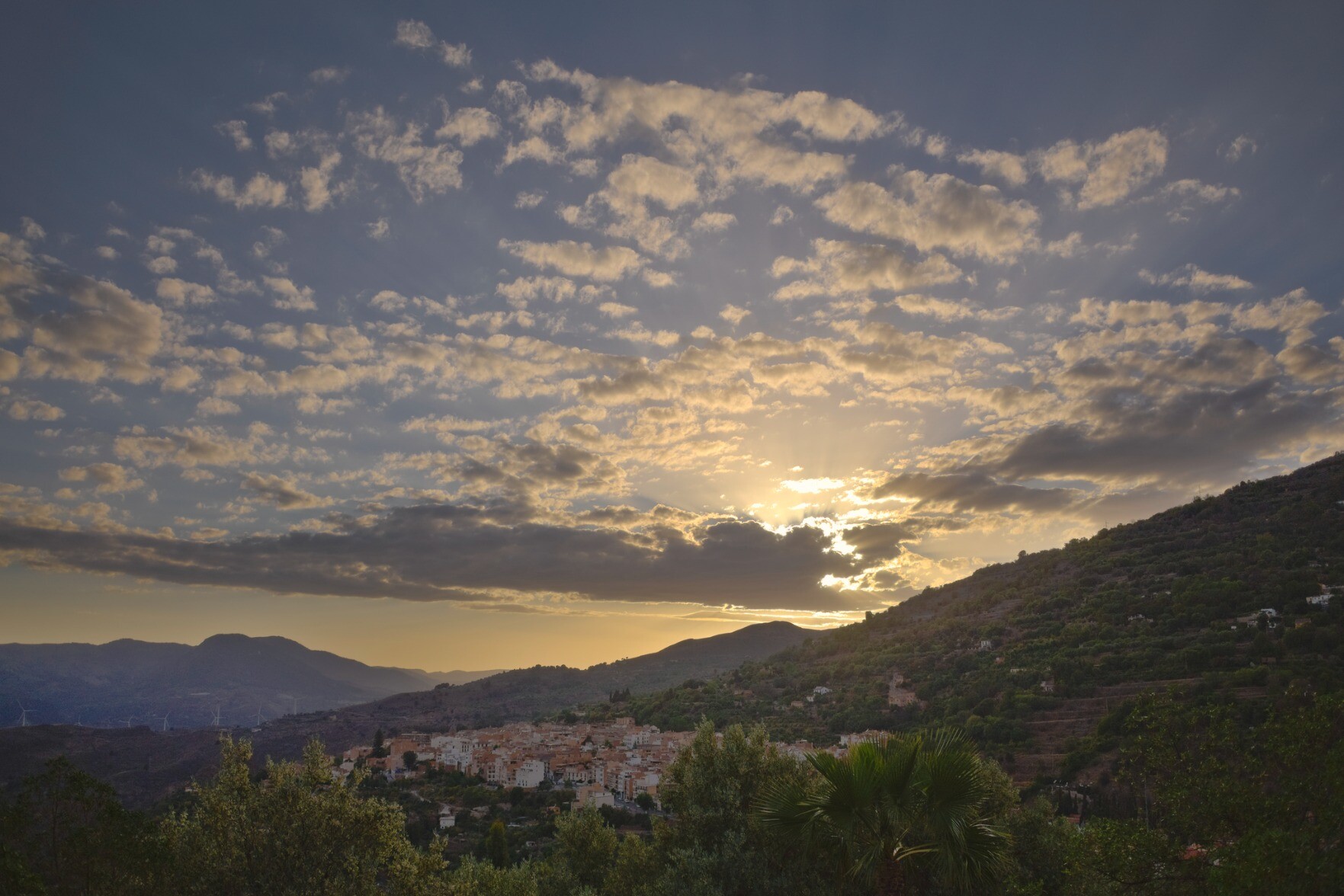A sky starts to turn yellow at sunset. The bottom part of the image has a spanish town enjoying the last rays of the sun.