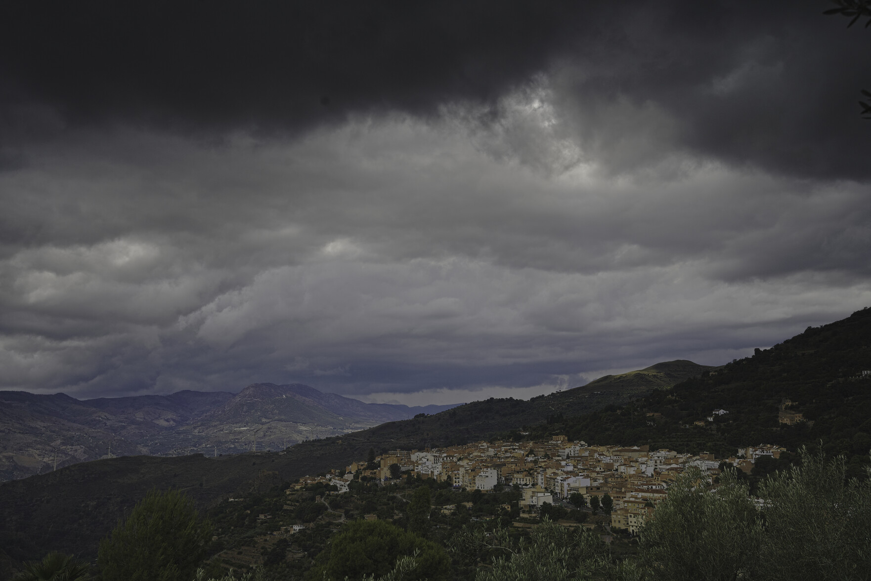 Some very dark thunder clouds are at the top of the image. below nestles a small town surrounded by green hillsides