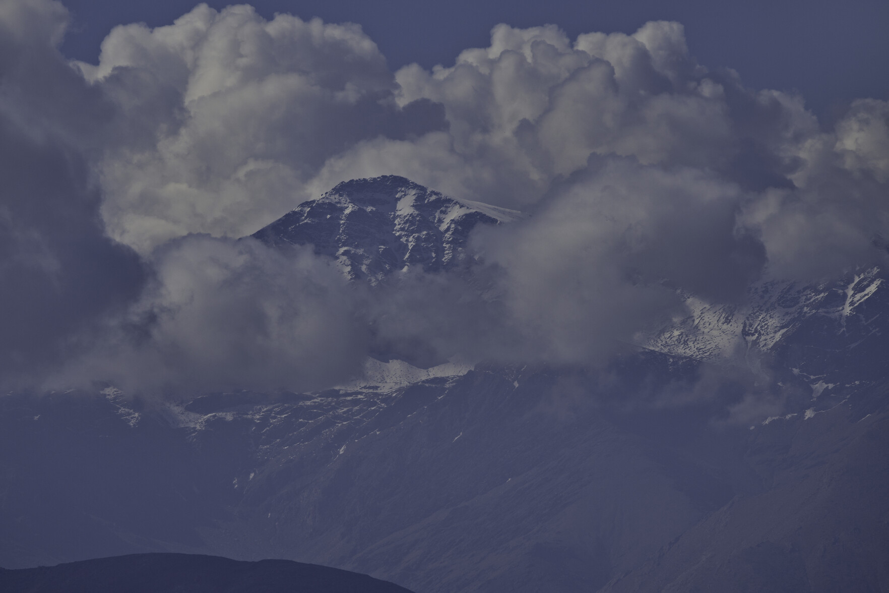 A mountain summit in snow emerges from the surrounding clouds