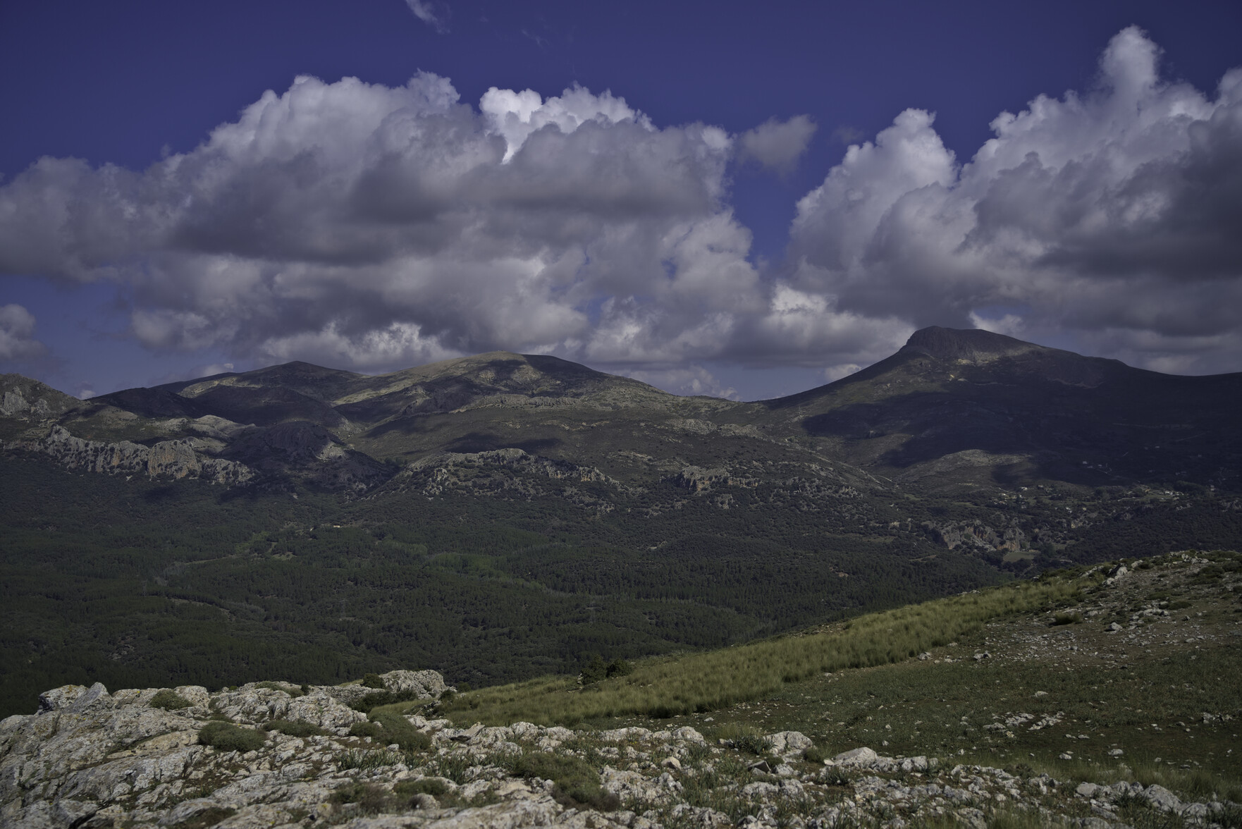 Some distant hills have big white clouds above them, surrounded by blue sky