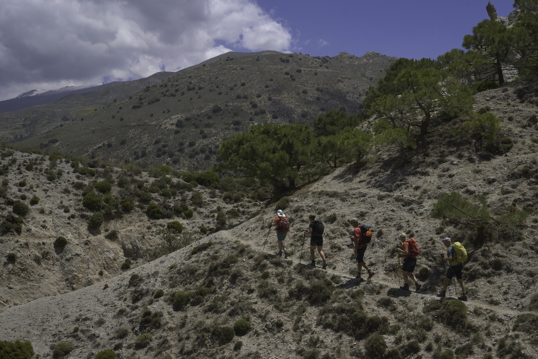 Hikers on a path with some green hills. Cloud and blue sky above