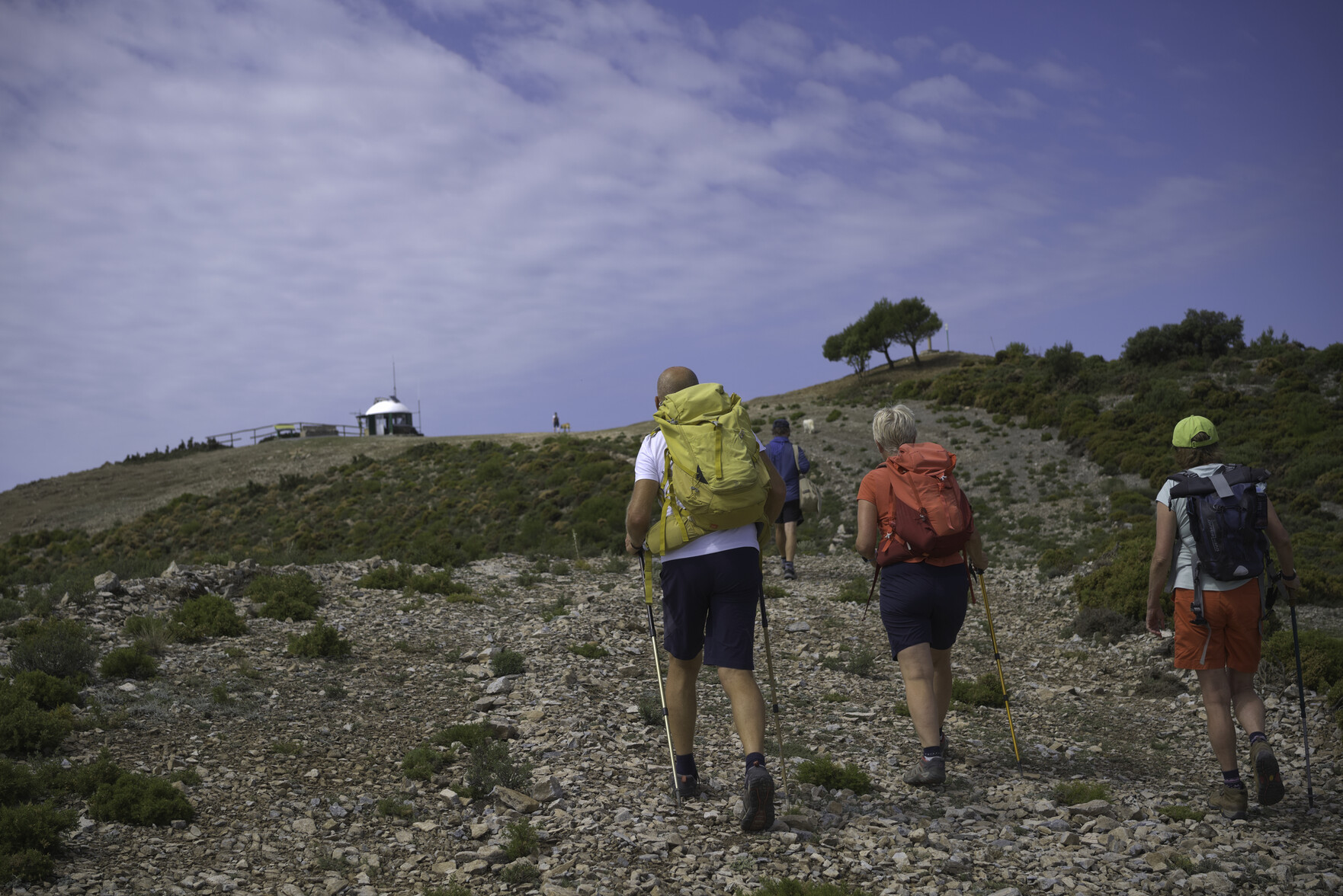 Hikers are approaching a summit of a peak which is marked by a white fire lookout post