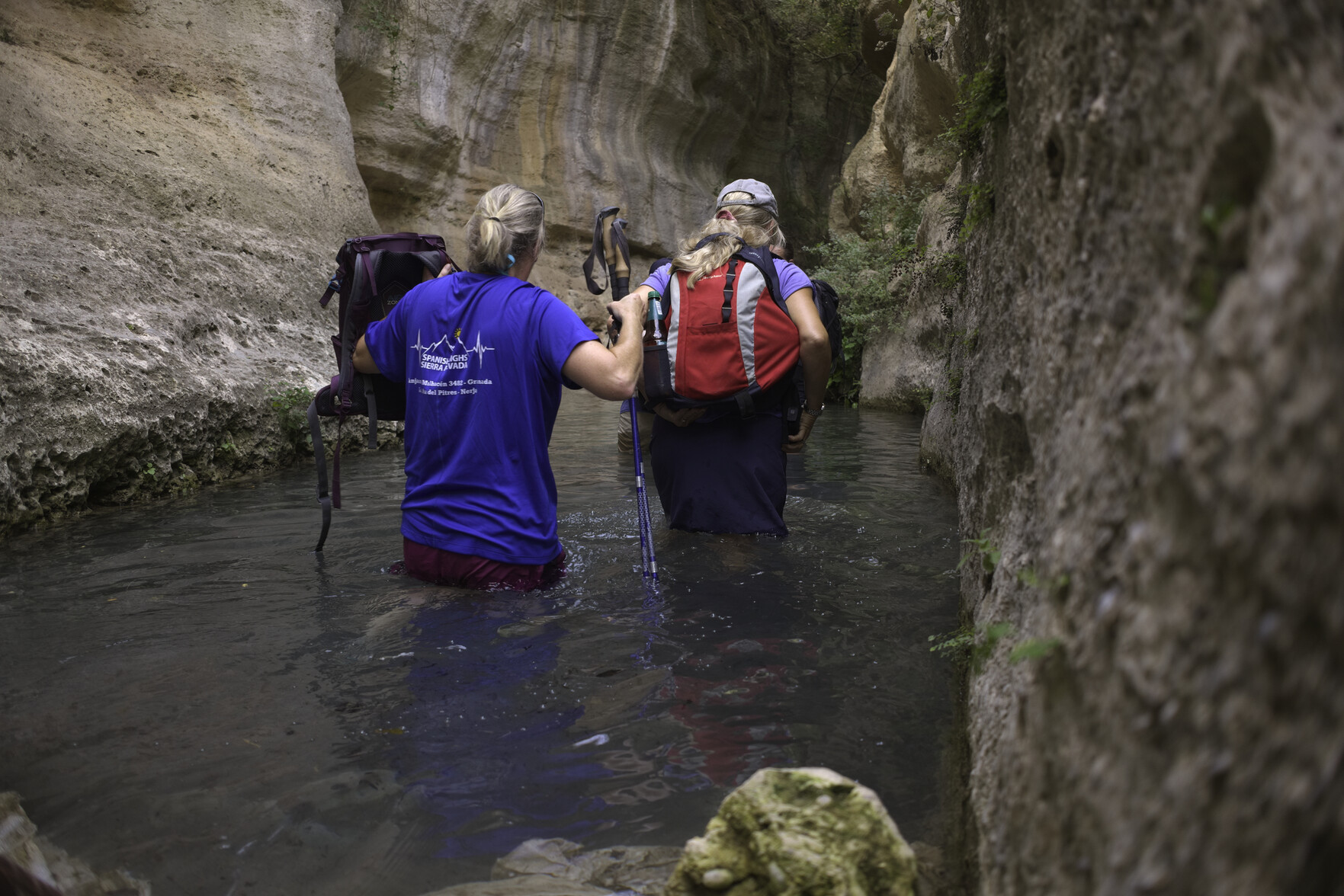 Two hikers are waist deep in a small lagoon within a steep sided dramatic gorge