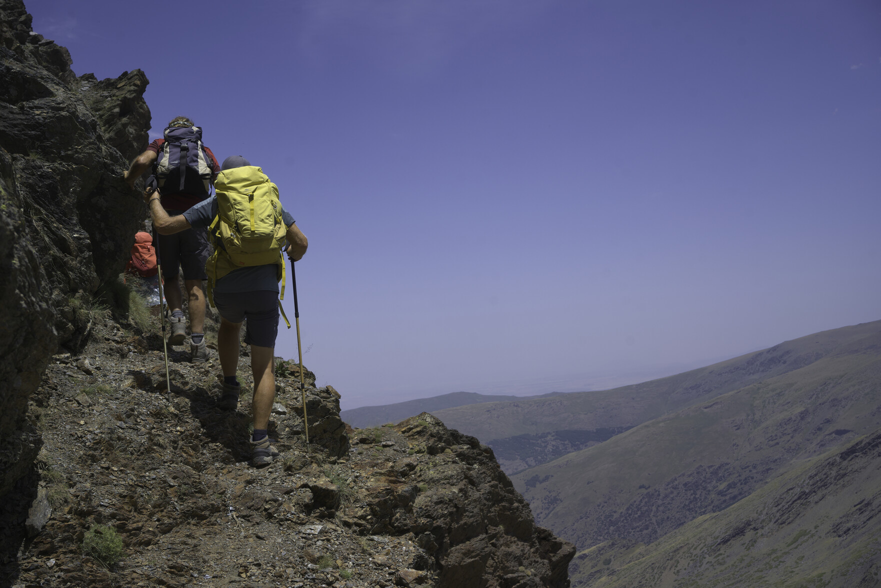 Two hikers walk along a narrow path with a steep drop off to the right
