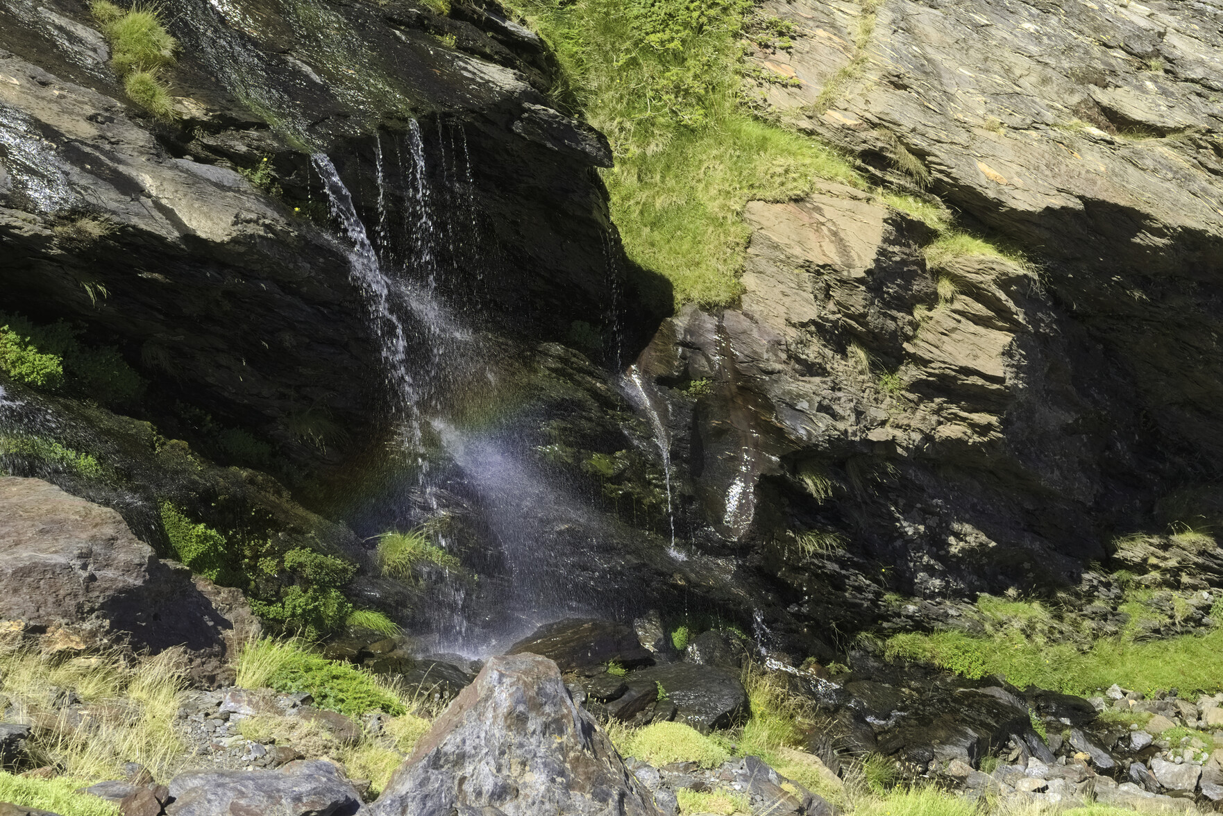 Water cascades over a fall to the left. Inside the waterfall a small rainbow can be seen