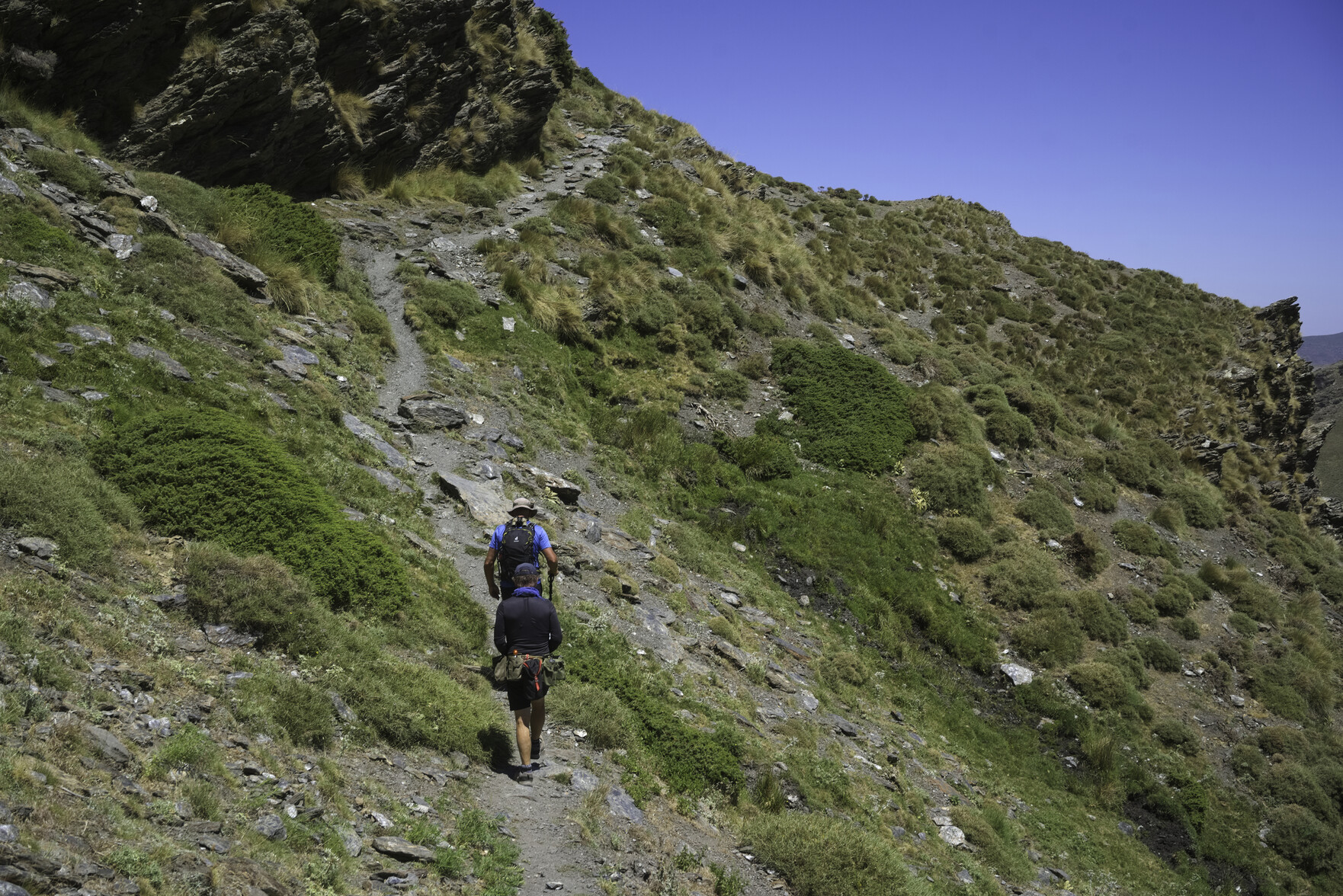 People ascend a narrow track up a mountainside