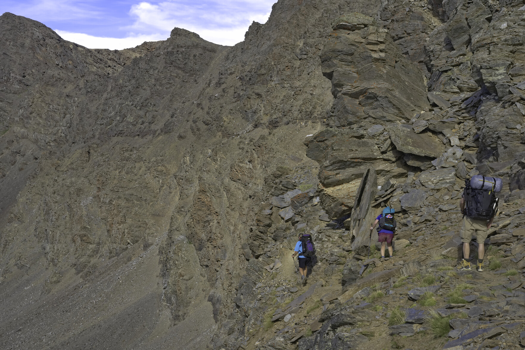 Some hikers walk along a narrow ledge across a mountain face