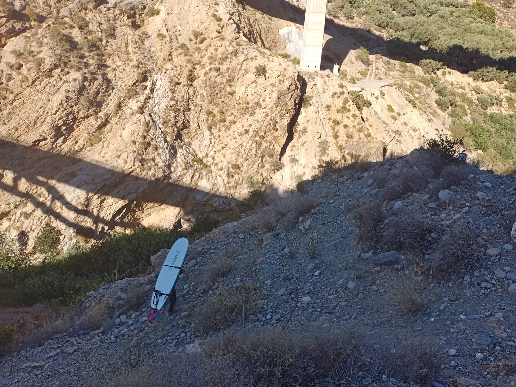A surfboard is being carried across a steep scree slope