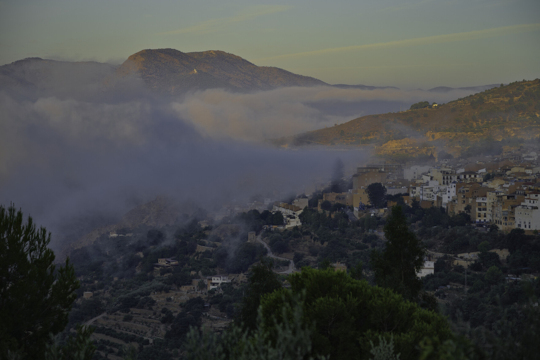 A spanish town sits awaiting the sun which is behind it. Some low clouds fill the top left of the image