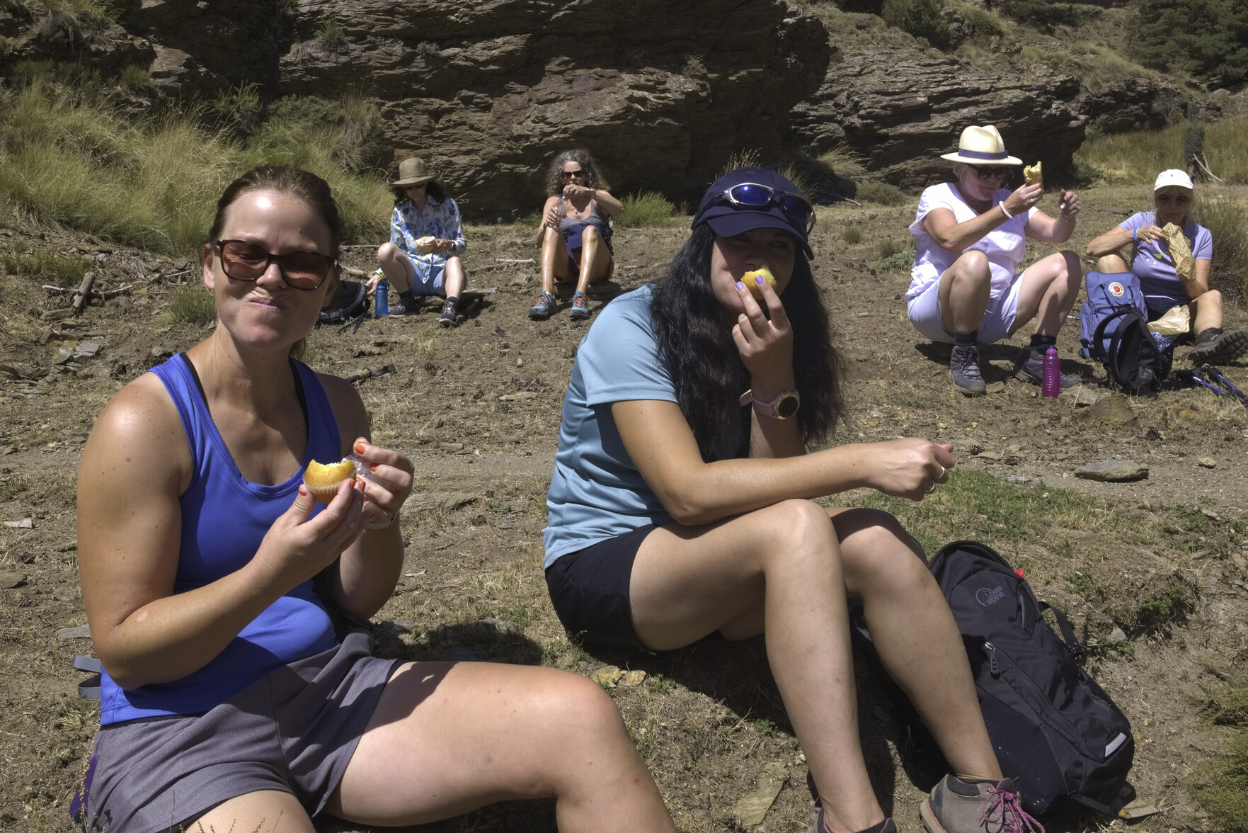 A group of ladies sit on some grass eating sandwiches