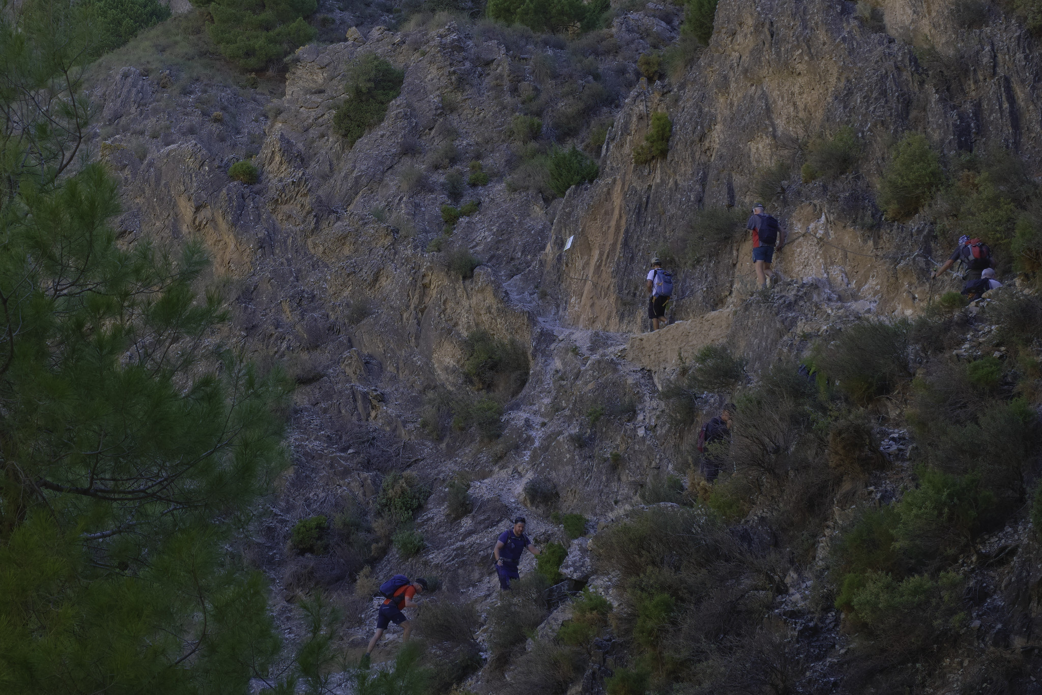 Walkers cling to a narrow mountain path equipped with chains