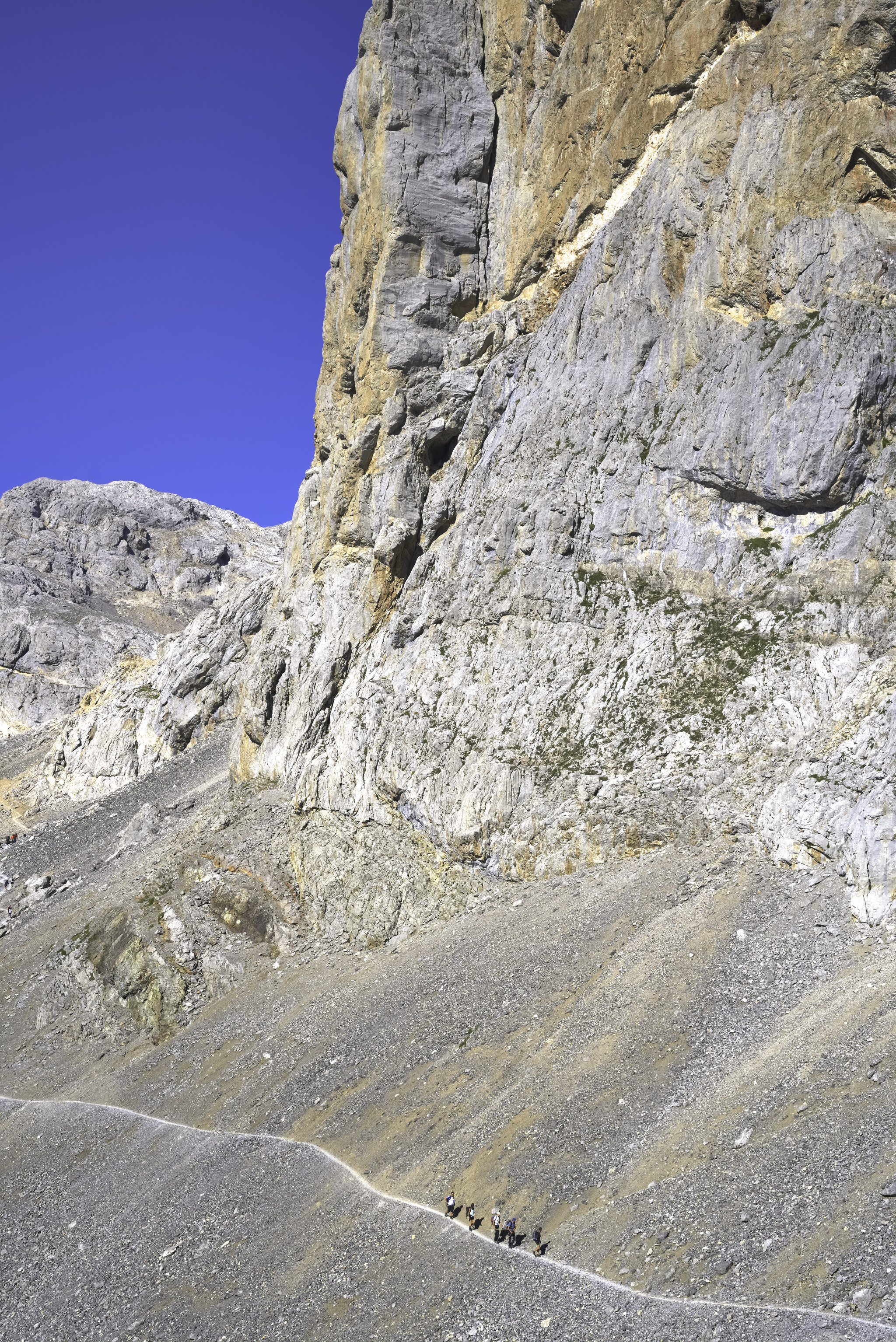 A group of 5 hikers walk below the massive cliffs of Peña Vieja in the Picos de Europa