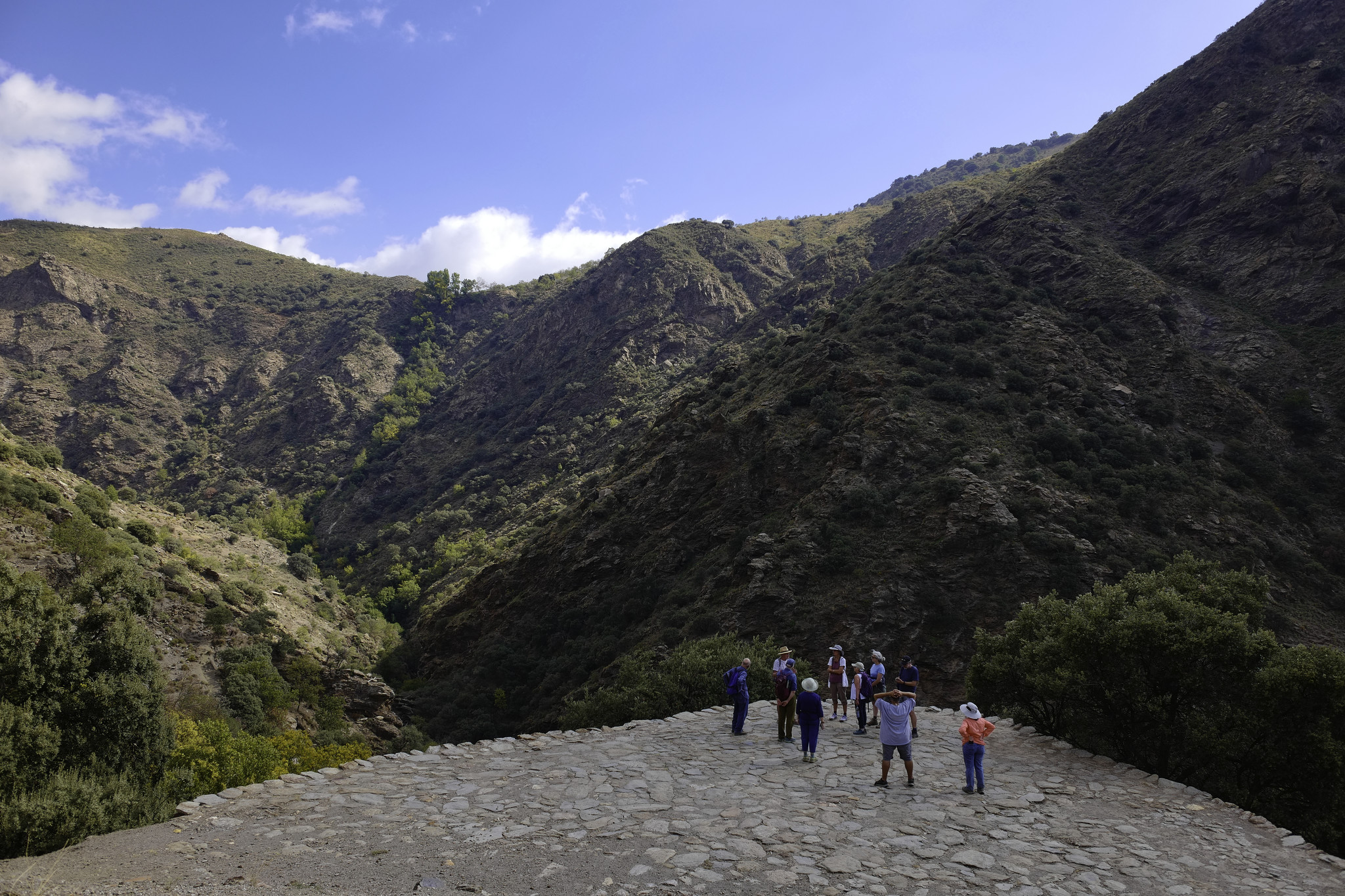 A group stand on an old "Era", an ancient threshing circle. Behind are steep hillsides with green shrub