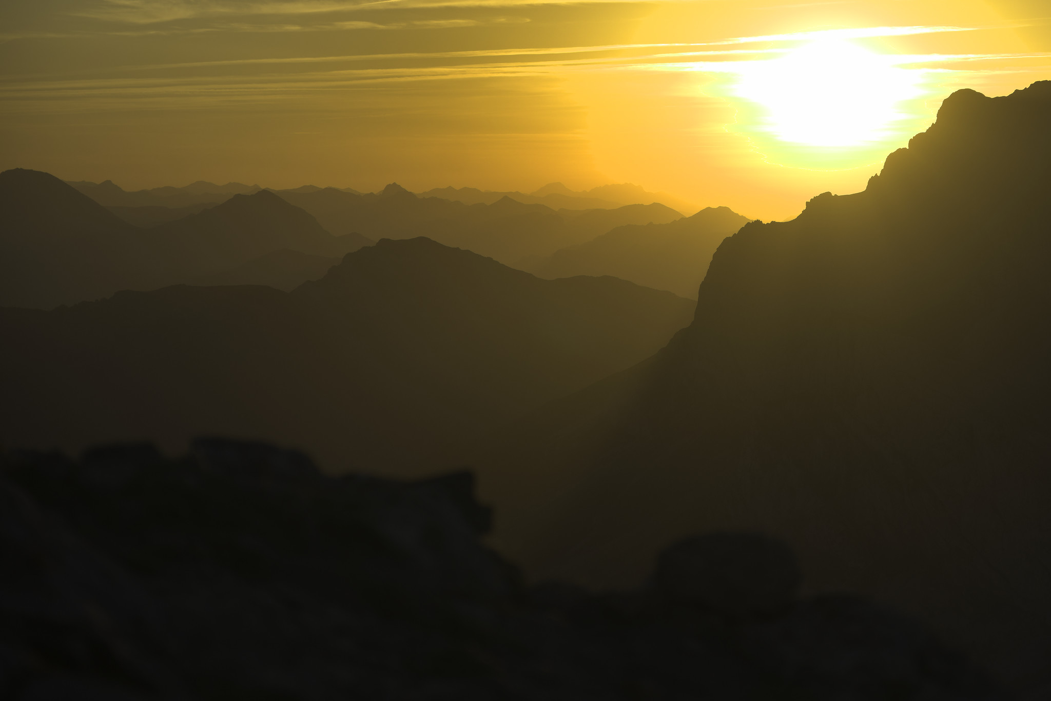 Lines of mountain ranges spread into the background with the setting sun just about to go behind a mountain peak