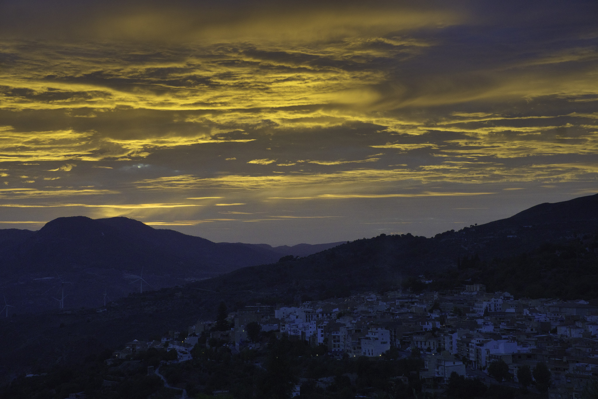 Golden light fills the sky at sunset. In the lower shadow lies a small spanish town