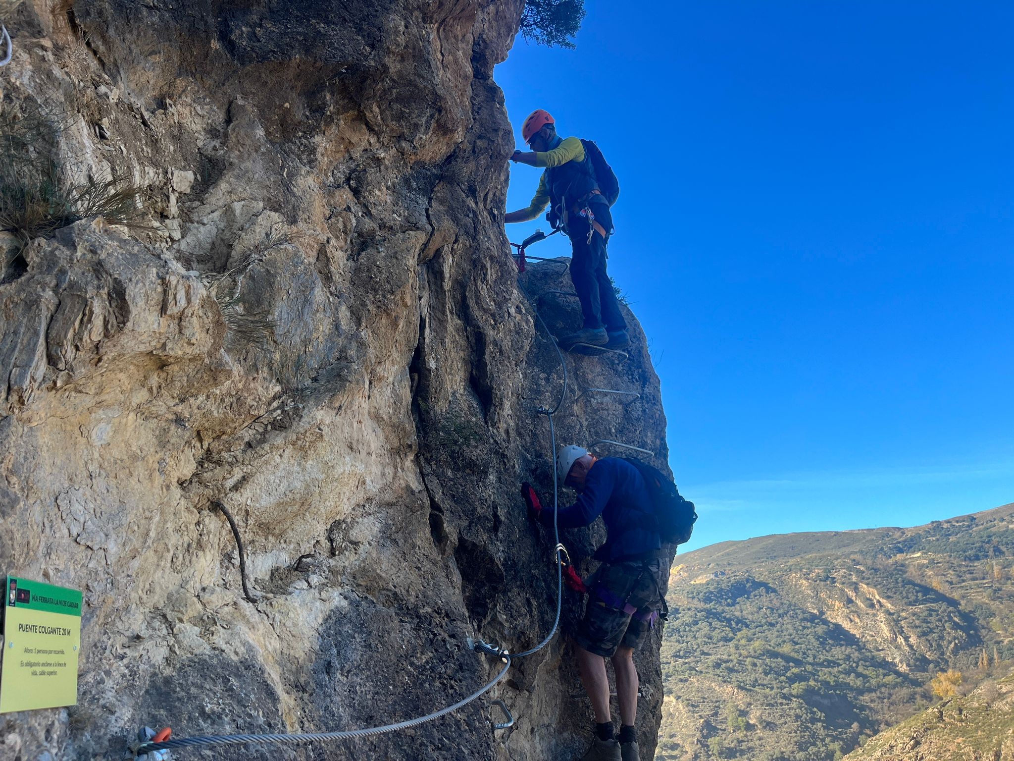 2 people ascend rungs of a via ferrata secured by chains and cables