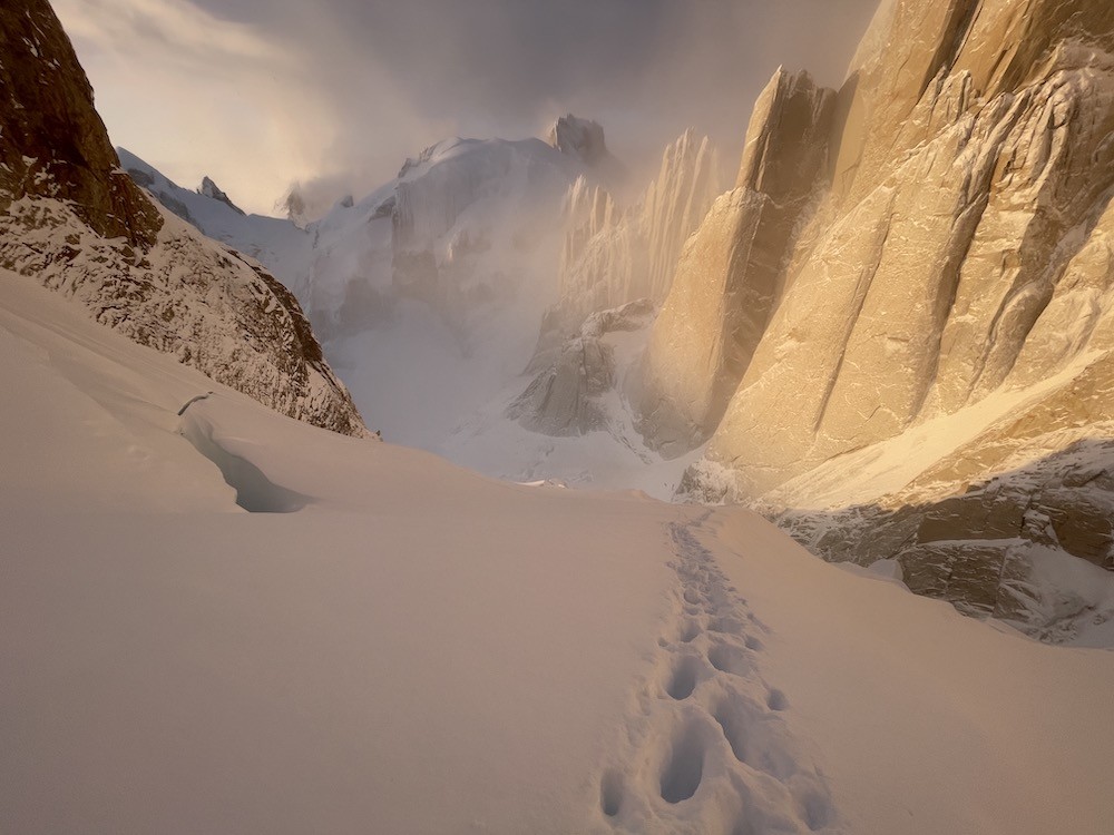 A winter mountain landscape with sunlit orange cliffs and white snow
