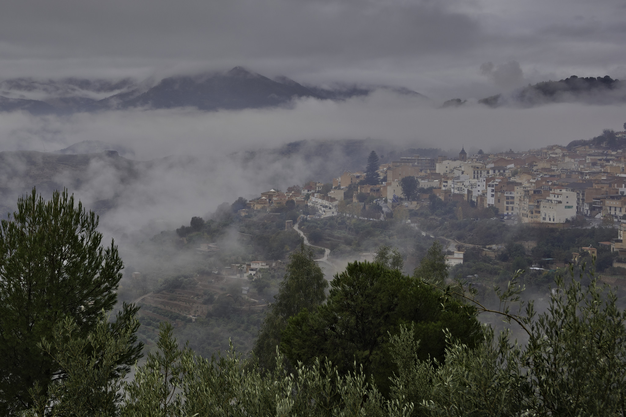 A town on the right emerges from low lying rain clouds set in layers above the town