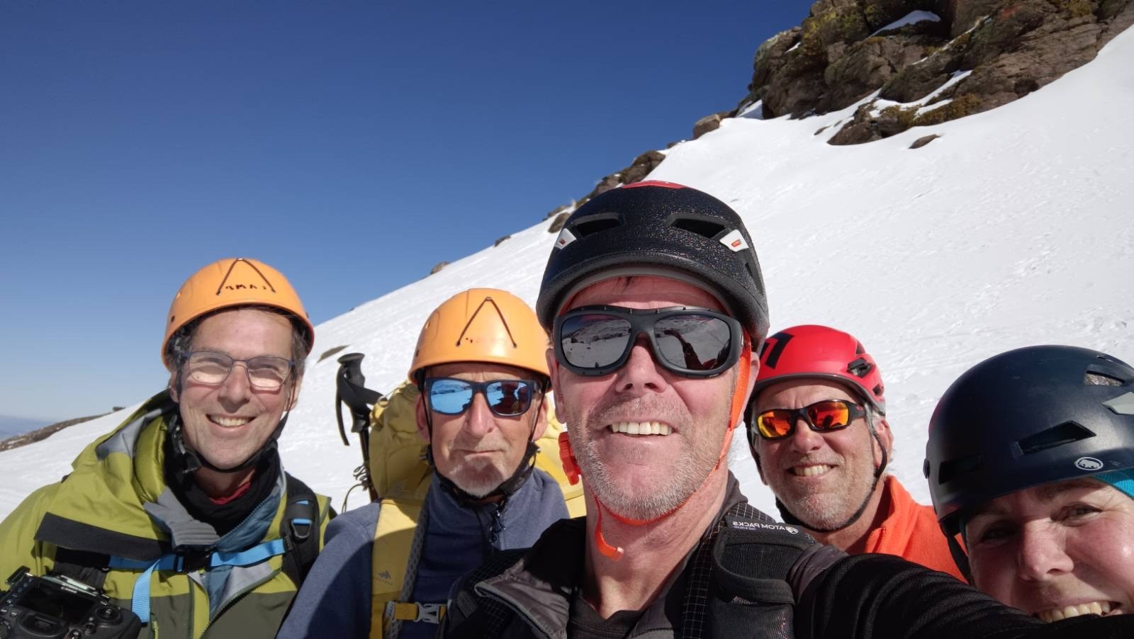 Five happy, smiling faces wearing helmets, are enjoying their day out in the snowy mountains