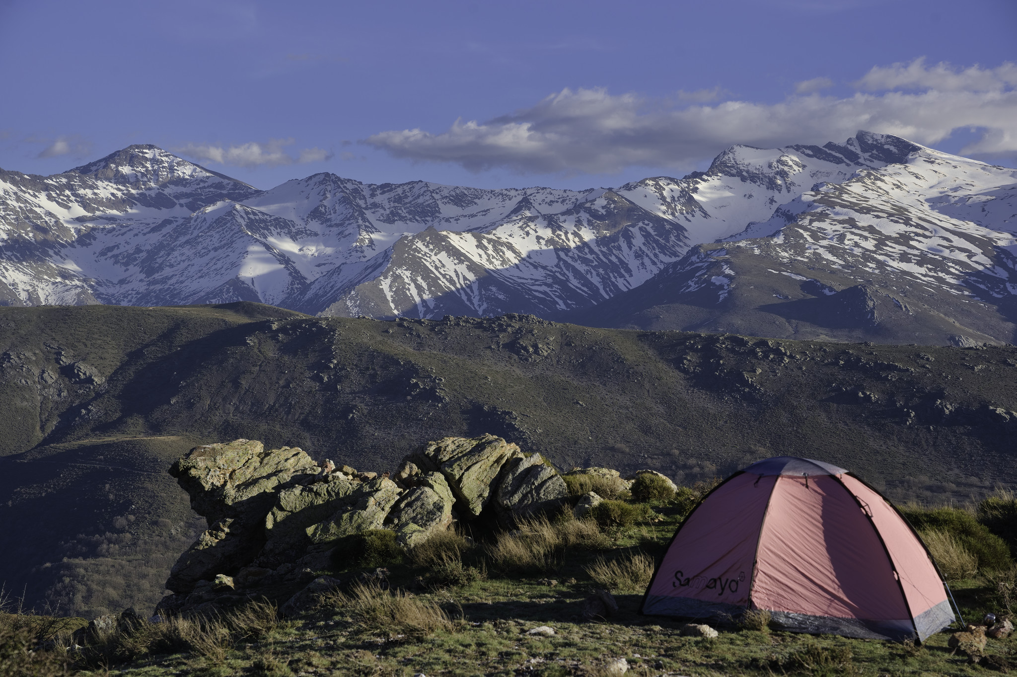 Campsite with a view! Center section of Sierra Nevada ridge from Mulhacen to Veleta

Some illuminated rocks in the foreground with a low lying ridge middle distance and some dramatic snow clad peaks beyond