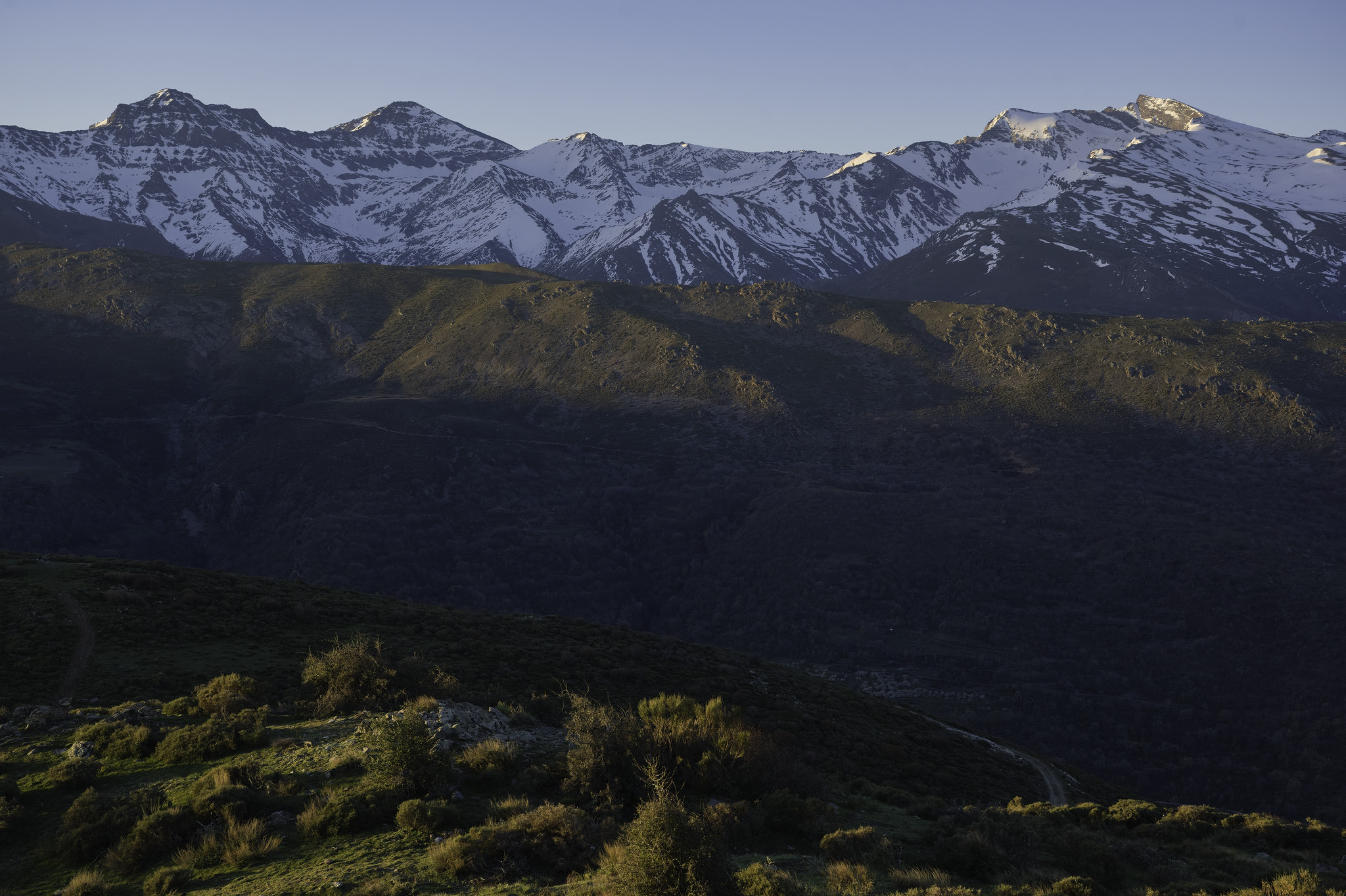 Morning light reaches the intervening ridges while in the background the sun reaches the summits of the peaks