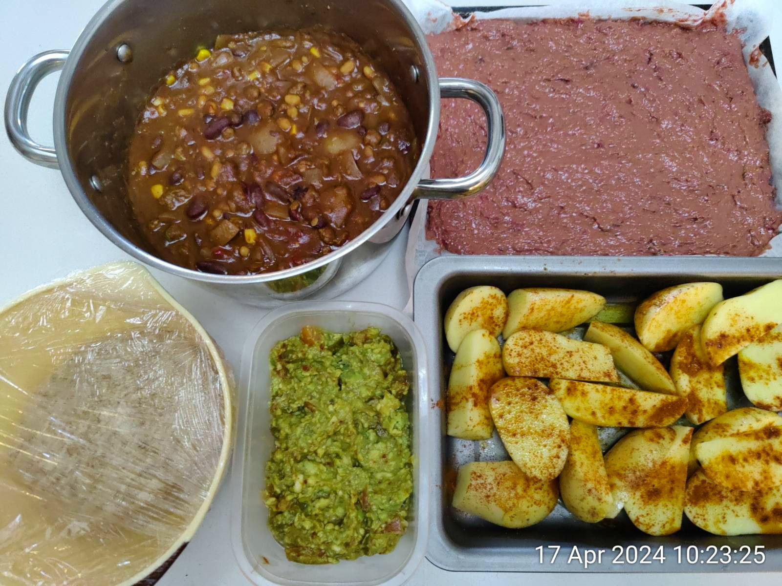 A selection of colorful food dishes being prepared including chili, guacamole, roast potatoes and bread