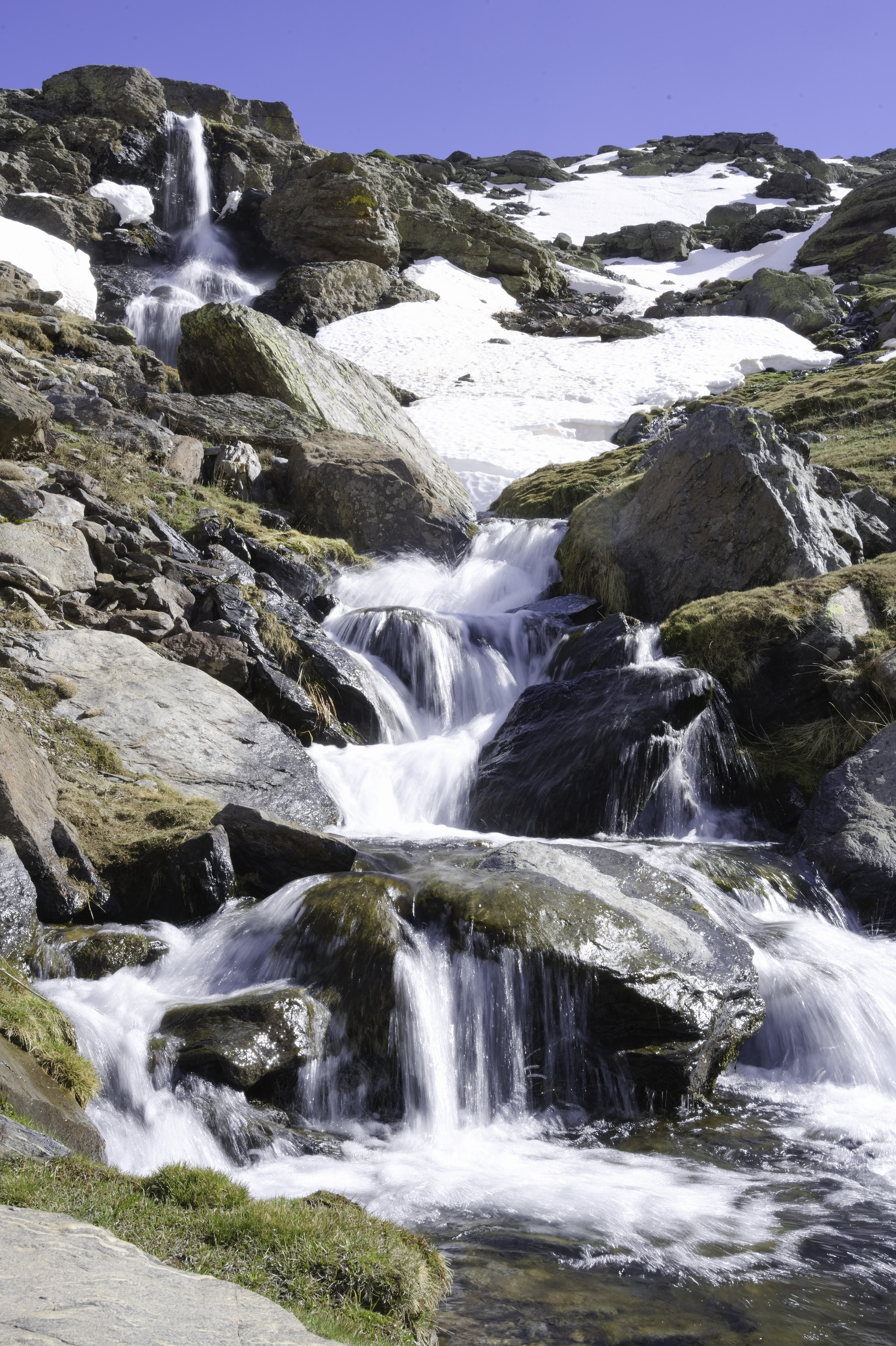 A series of waterfalls tumbles down over cliffs in Spains Sierra Nevada. Some snow patches are seen either side of the waters