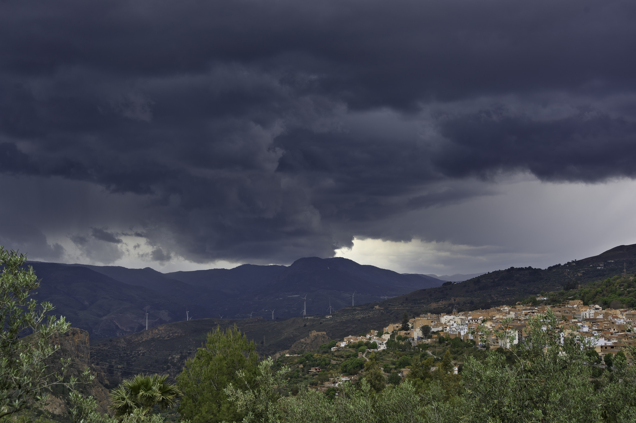 Some dark threatening clouds brings a storm. below is a small spanish town with green trees