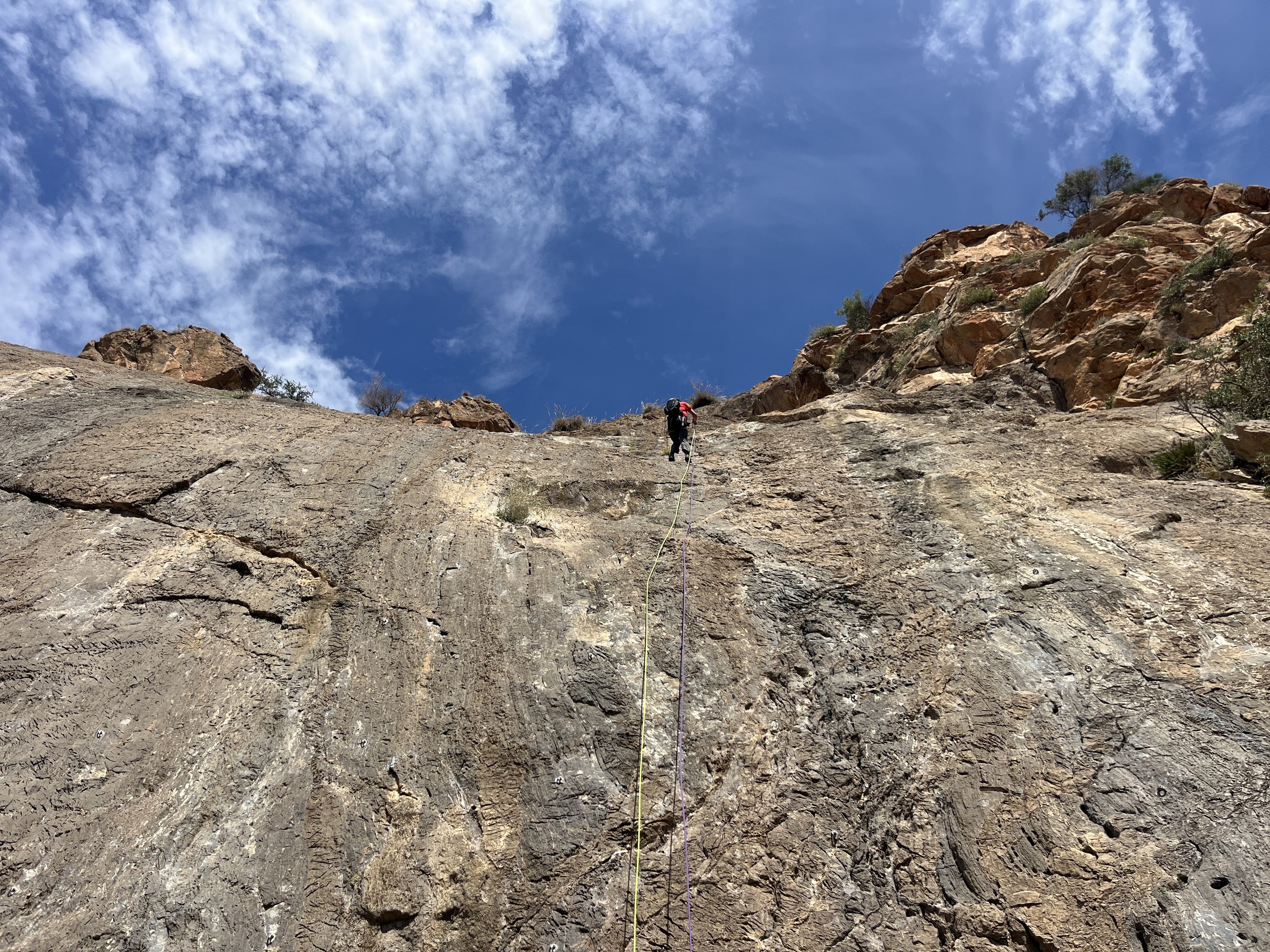 A person in red abseiling down a vertical rock slab. Blue sky above